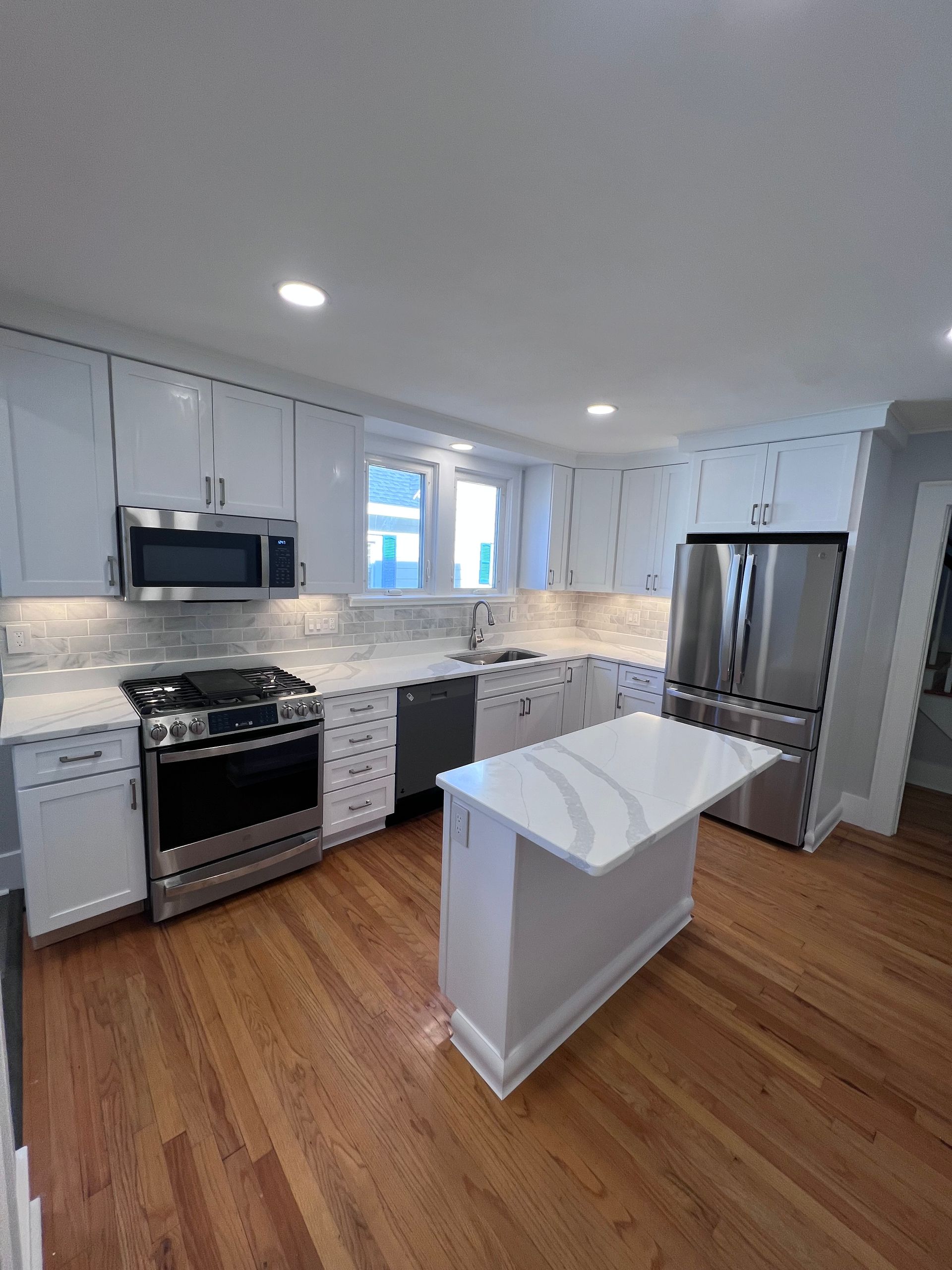 Bright modern kitchen with white cabinets, stainless appliances, and a small island on wood floors
