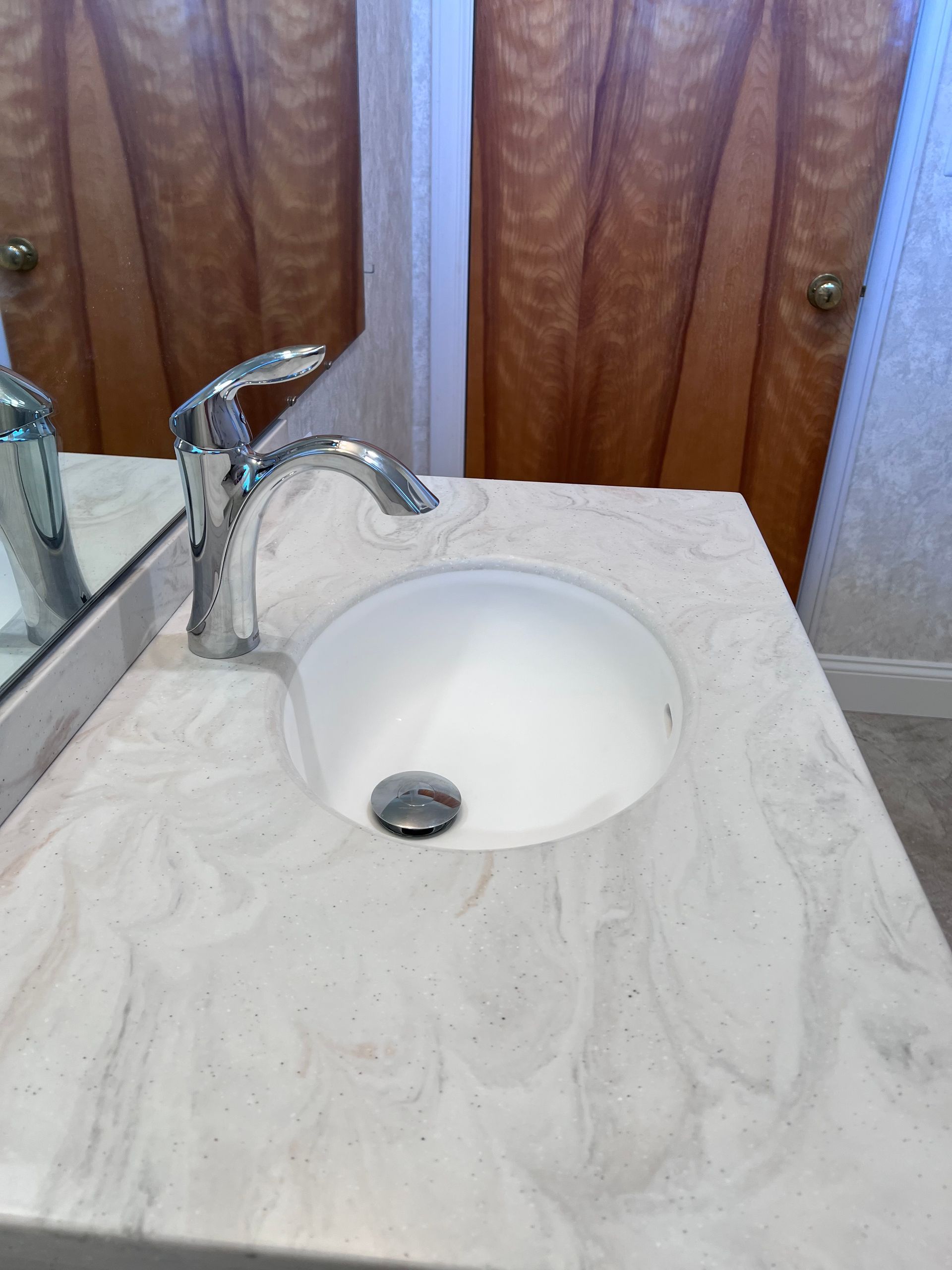 Bathroom sink with chrome faucet and light marble countertop in front of wooden cabinet doors