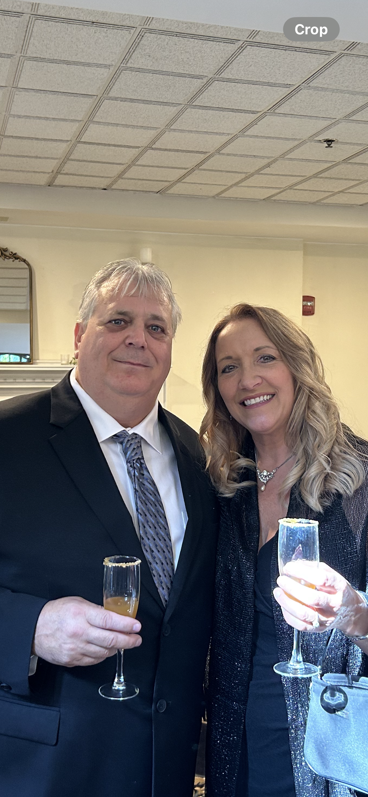 Two people in formal attire smiling and holding drinks at an indoor event