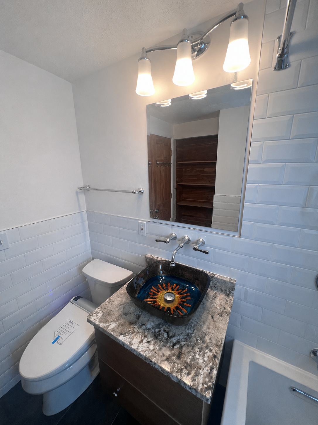 Small bathroom with toilet, granite sink vanity, mirror, and overhead lights.
