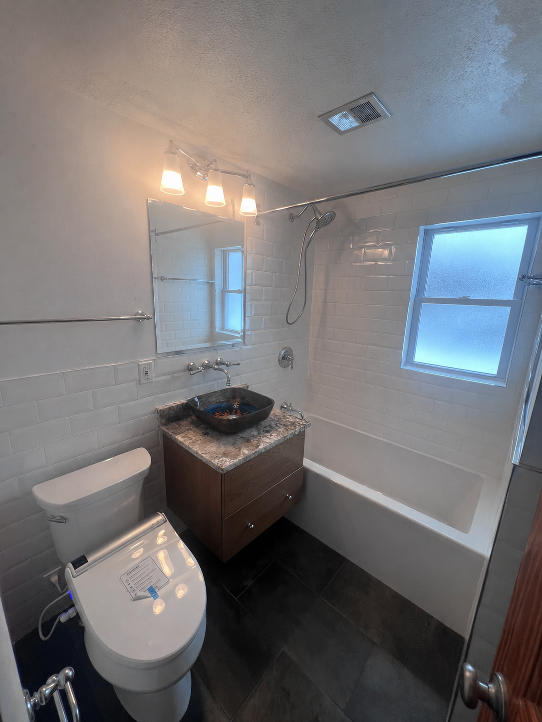 Small bathroom with toilet, vanity sink, bathtub, white tile walls, and dark floor.