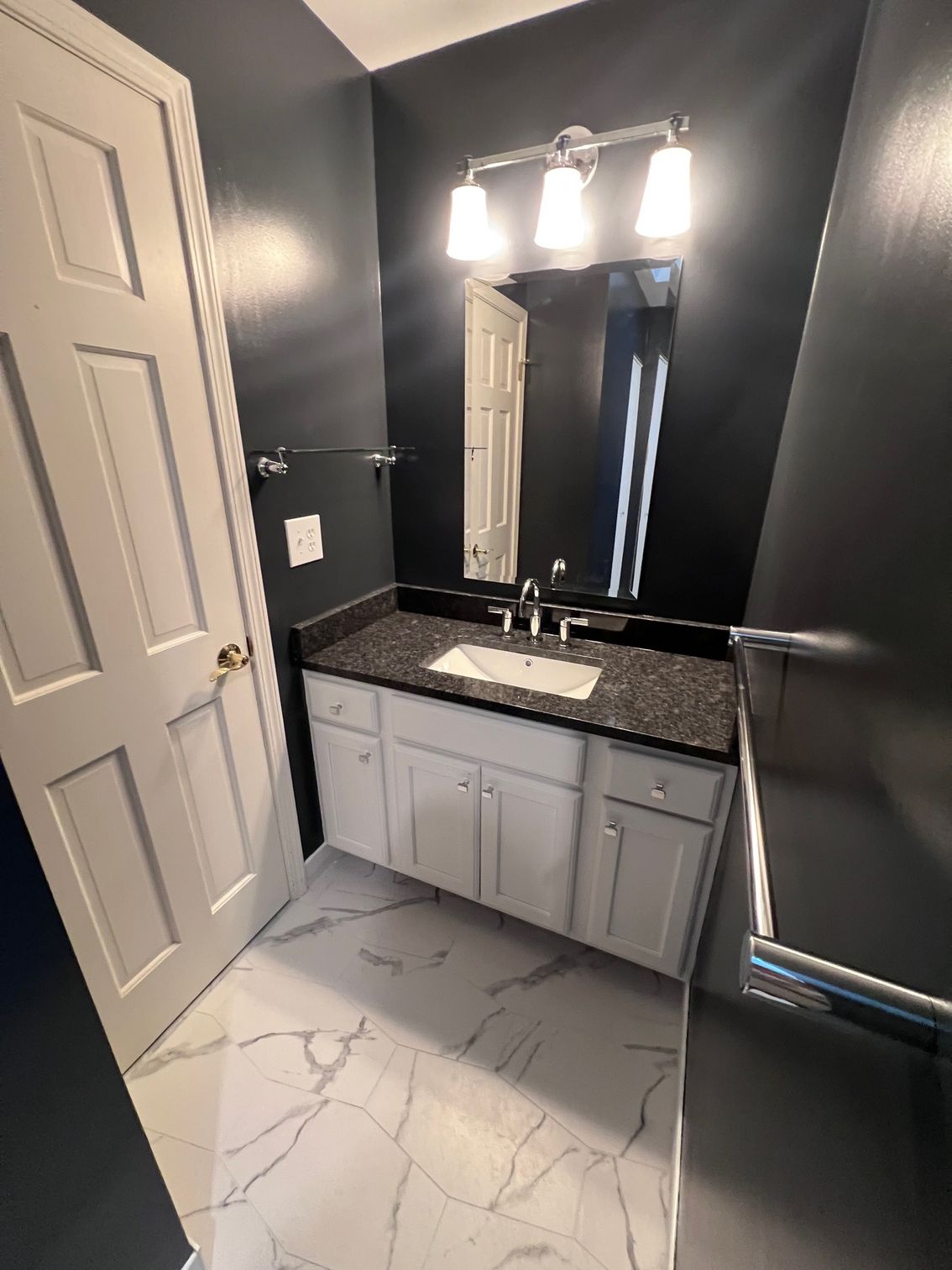 Modern bathroom with dark walls, white vanity, black countertop, mirror lights, and marble-look tile floor