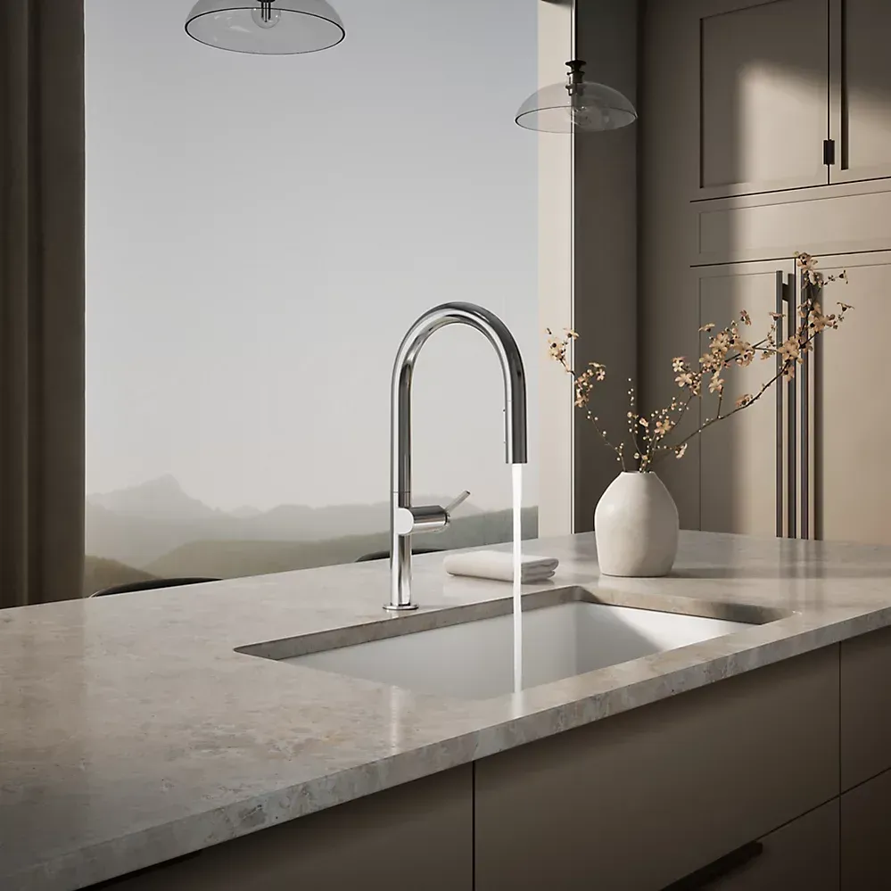 Modern kitchen with marble island, chrome faucet, pendant lights, and a vase of branches by a sunlit window