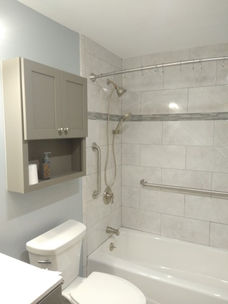 Accessible bathroom with tub-shower, grab bars, toilet, and wall-mounted cabinet.