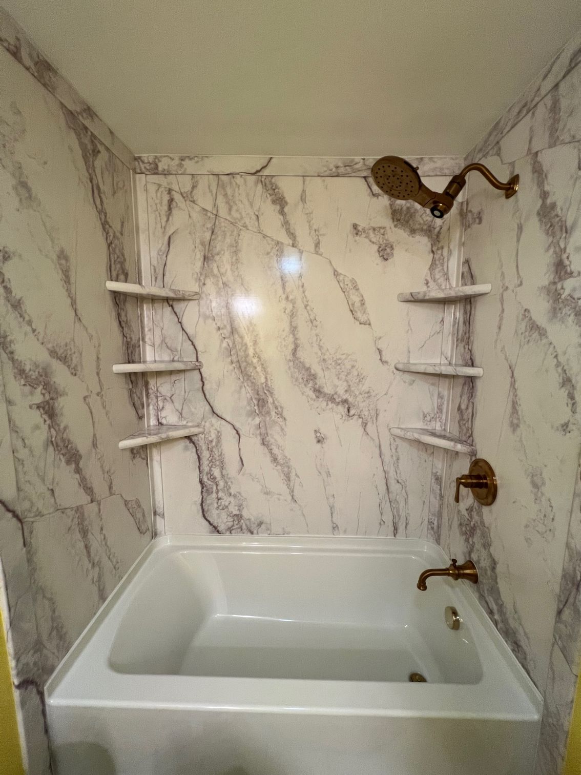 White marble-tiled bathtub alcove with built-in corner shelves and brass fixtures