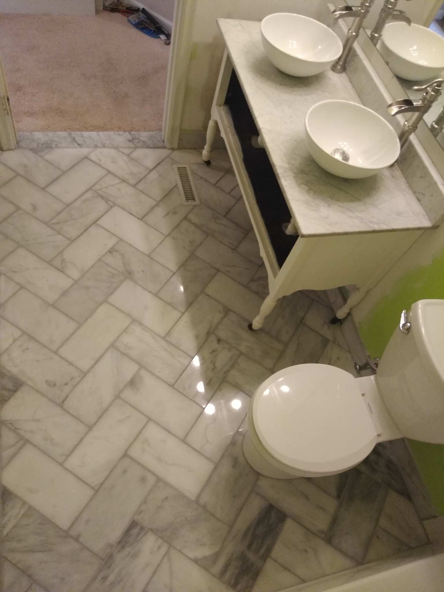 Bathroom with herringbone tile floor, double sinks, a toilet, and a vanity cabinet near a shower.