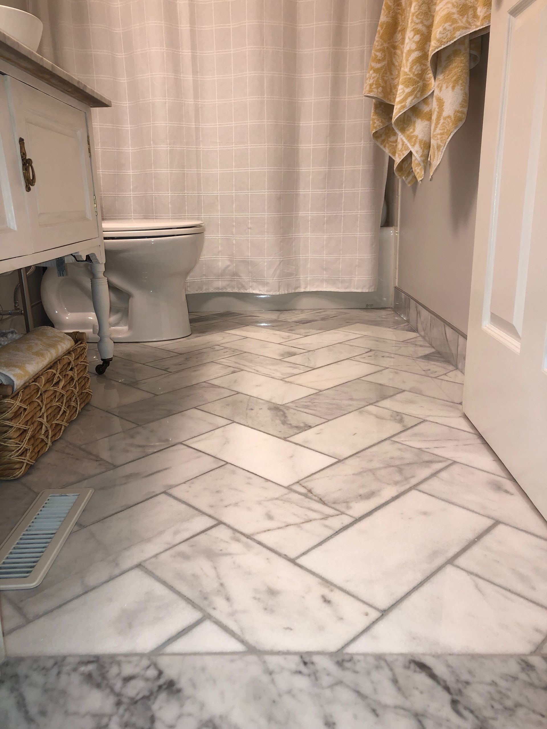 Bathroom with white marble tile floor, toilet, vanity, shower curtain, and a beige towel hanging on the right.