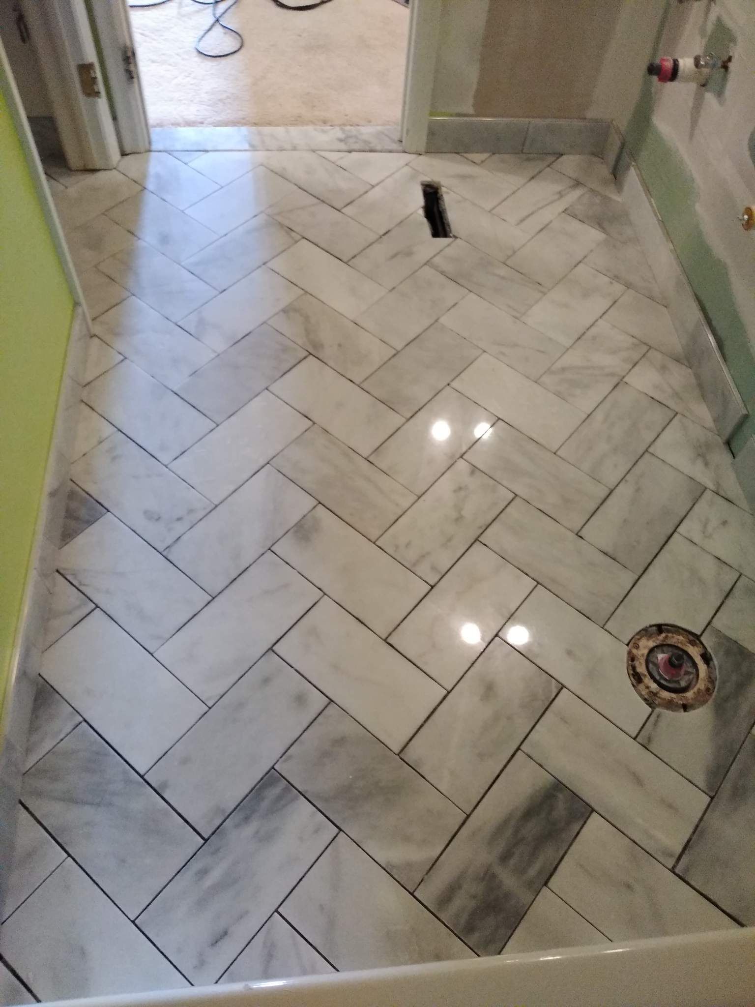 White herringbone tiled bathroom floor with a shower drain and a small black object near the center.