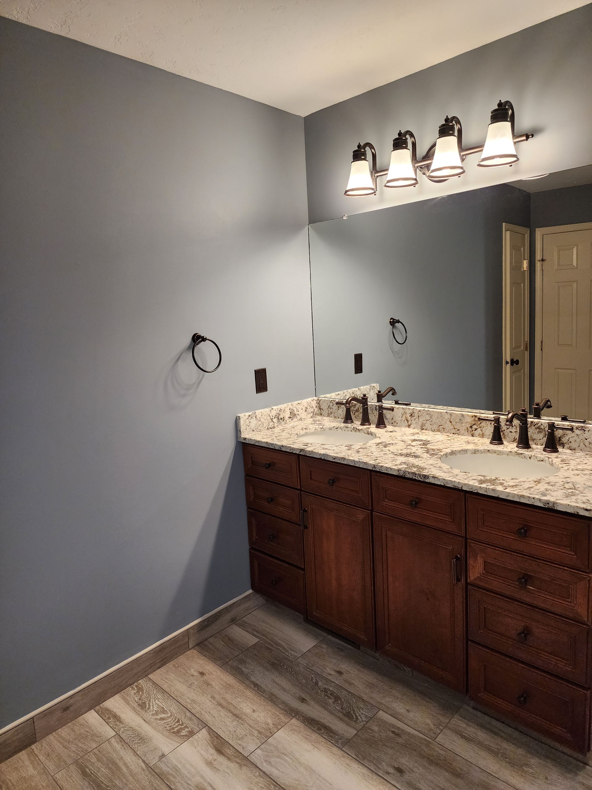 Bathroom vanity with granite countertop, wood cabinets, large mirror, and gray walls