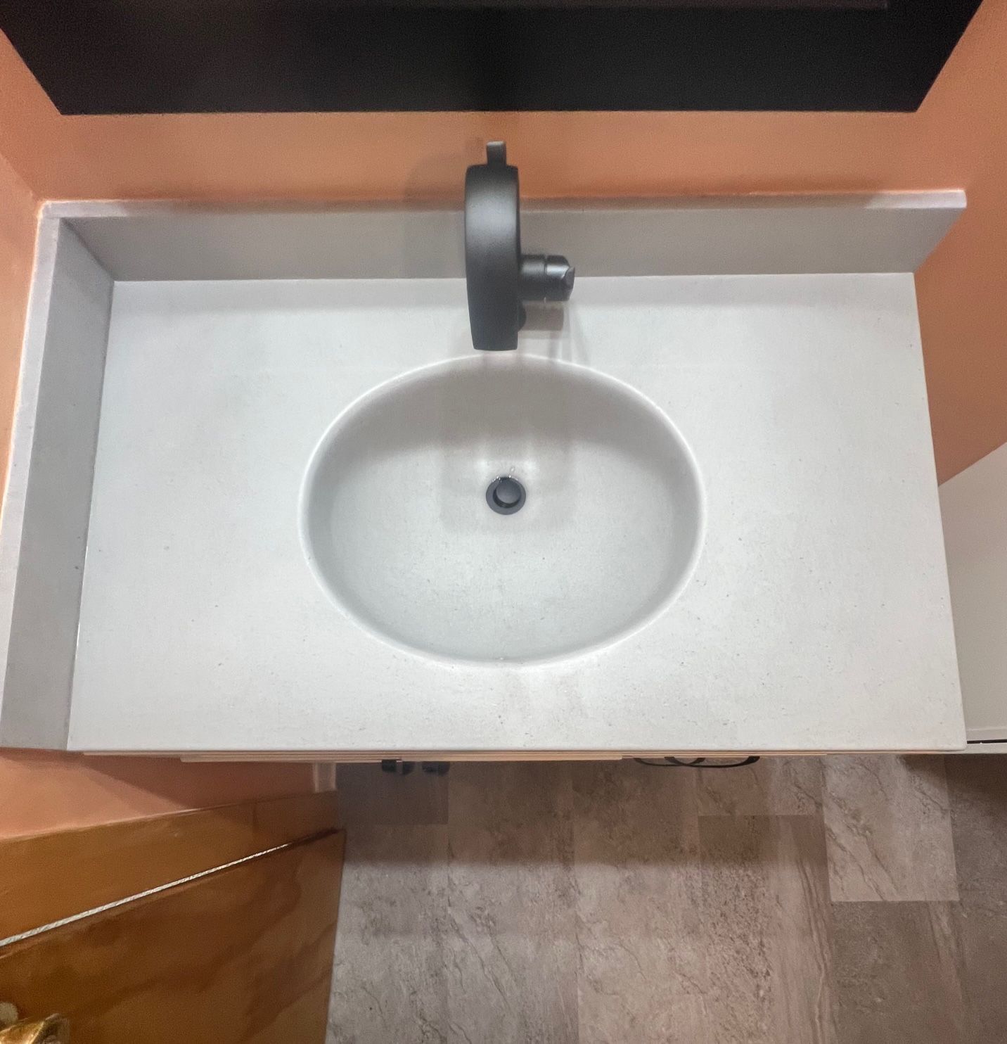 Overhead view of a white bathroom sink with a black faucet in a light-colored countertop.