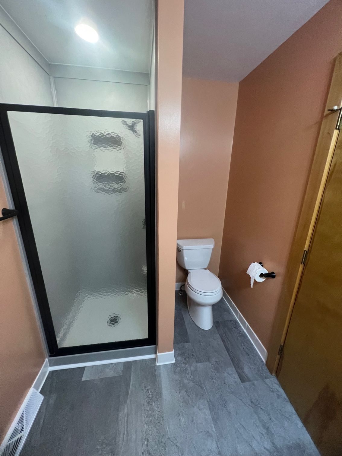 Small bathroom with shower stall, toilet, and orange walls on gray tile floor.