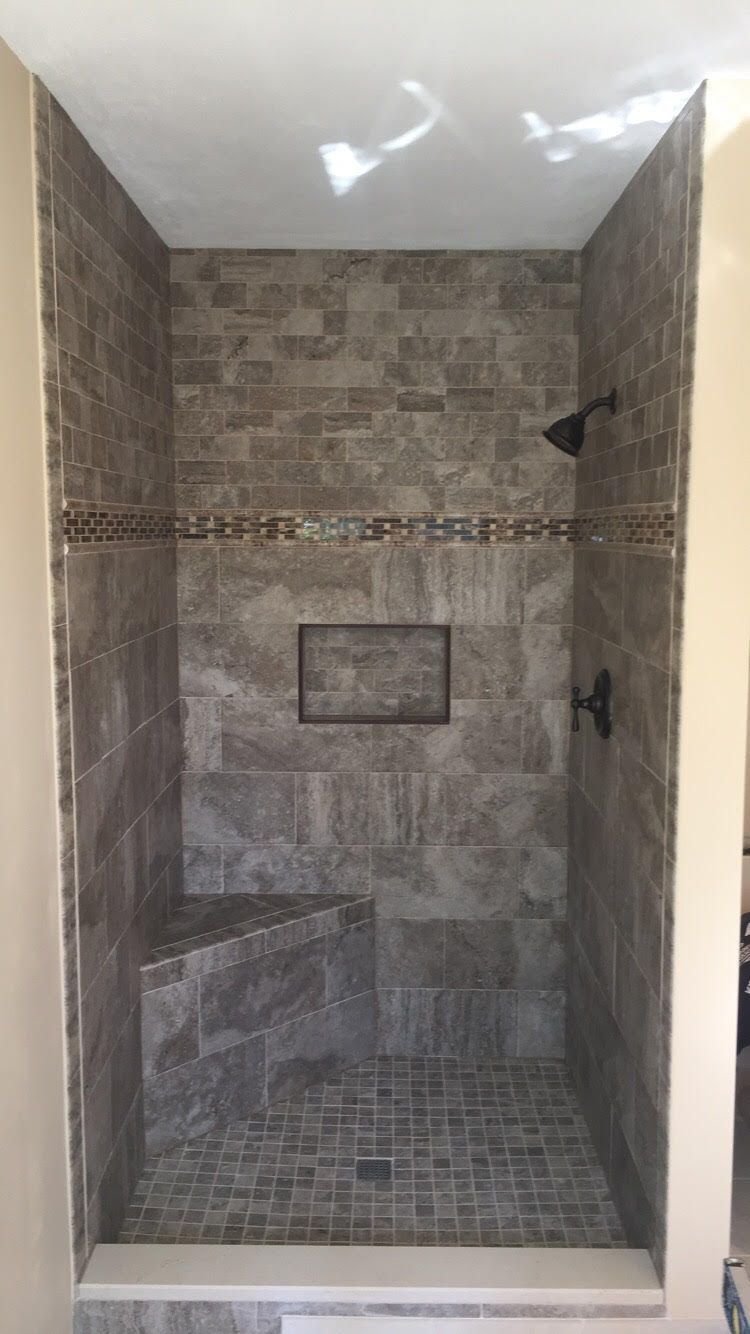 Empty tiled walk-in shower with bench, built-in niche, and dark showerheads under a white ceiling