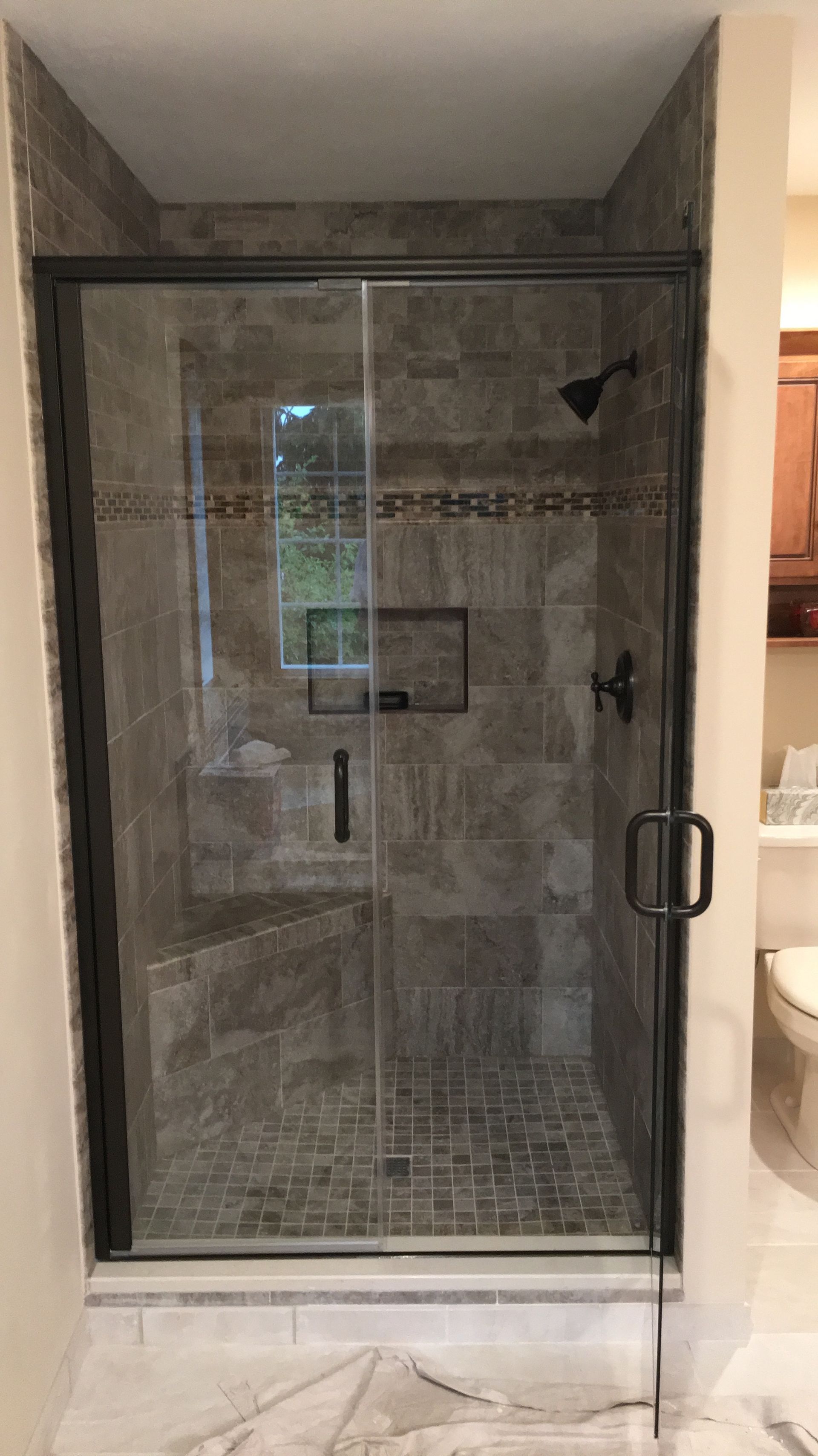 Walk-in shower with gray tile, glass door, and chrome handle in a bathroom alcove