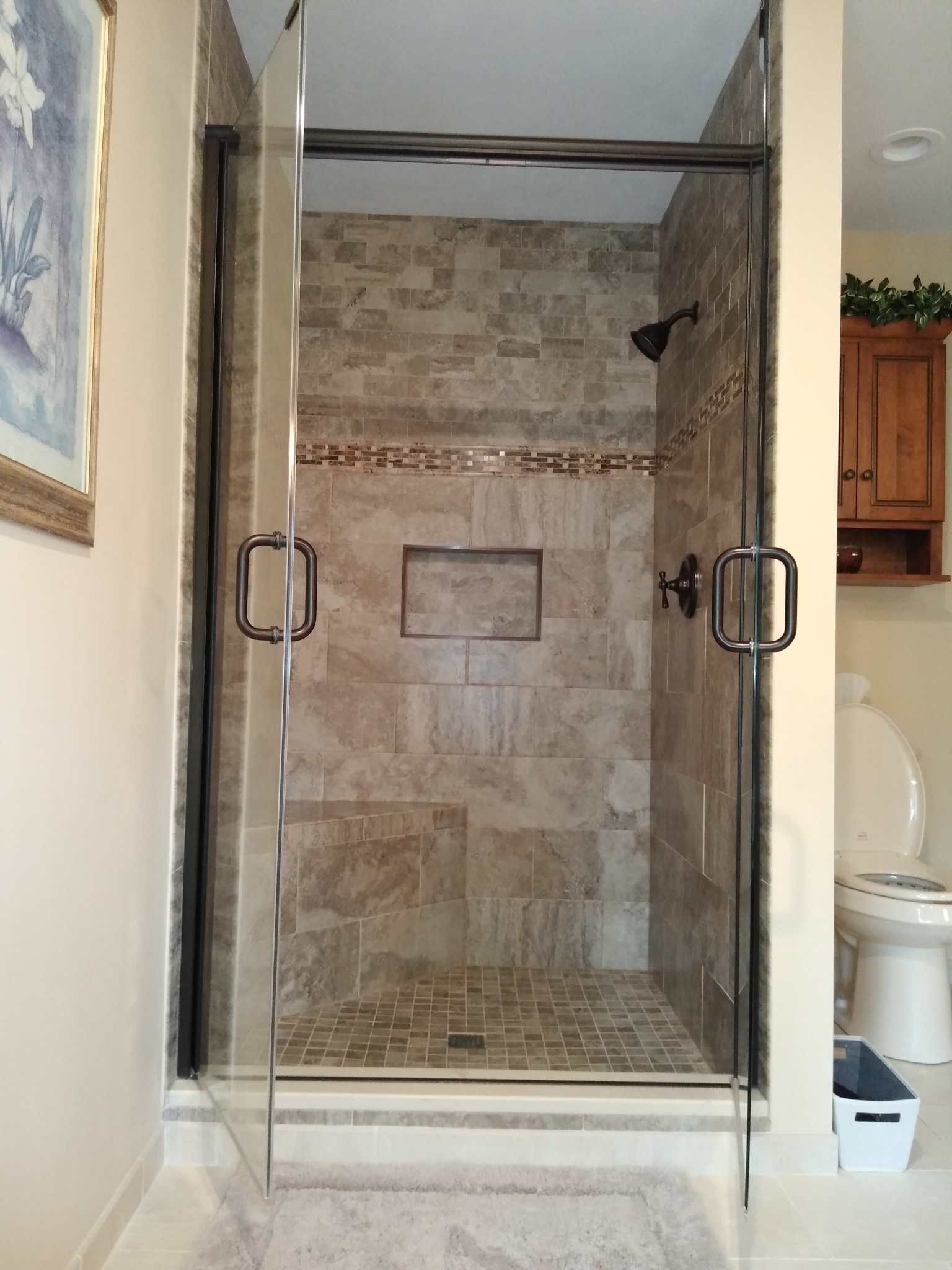 Glass shower enclosure with tiled stone walls in a bathroom