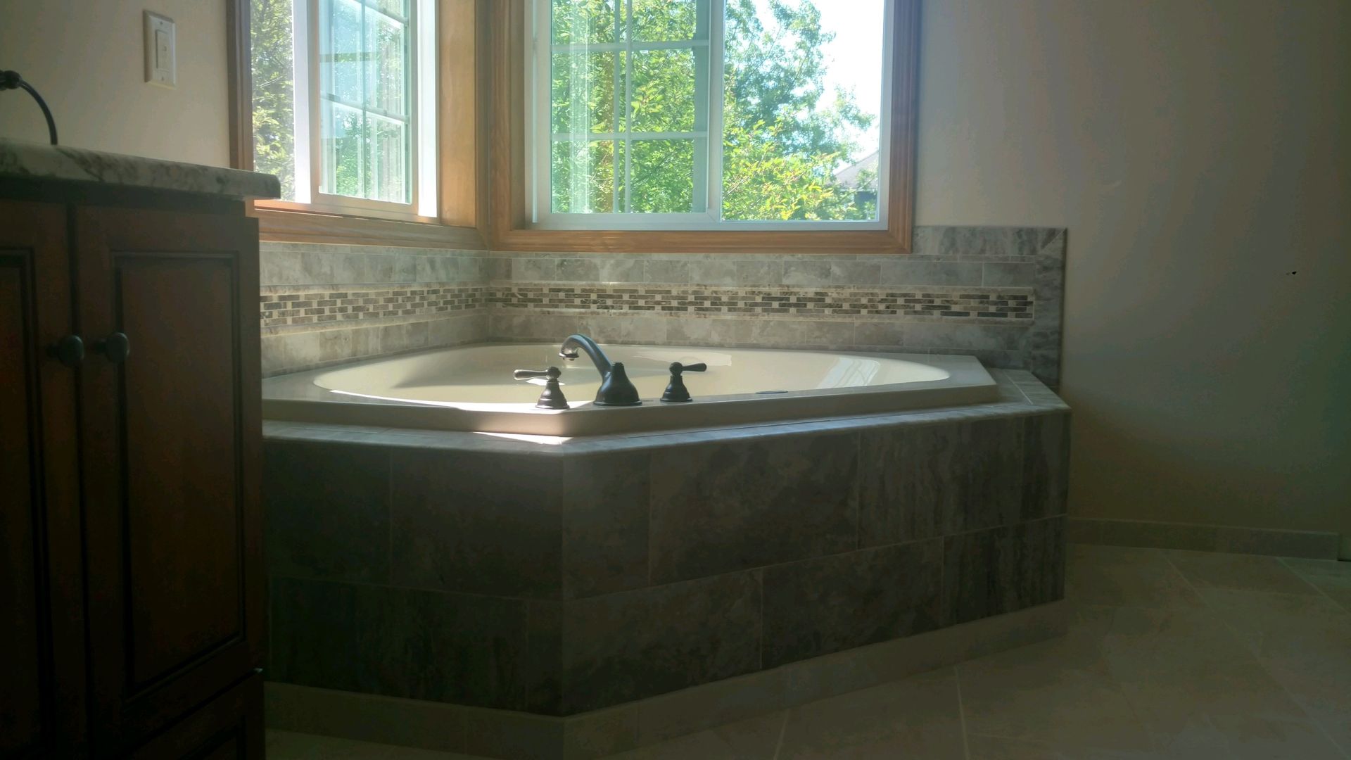 Sunlit bathroom with a corner soaking tub beneath a window and tiled surround