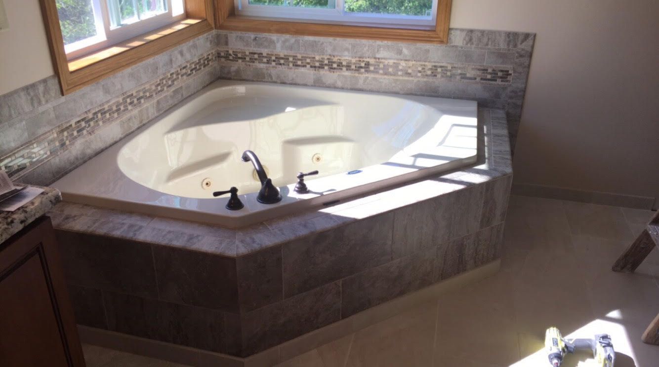 Large corner bathtub with chrome fixtures beside windows in a tiled bathroom