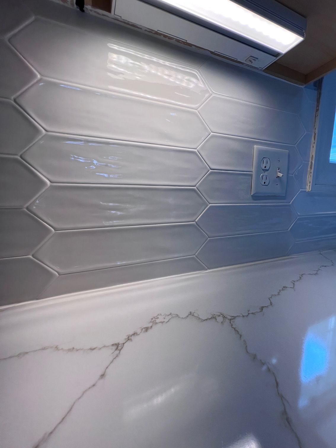 Modern kitchen backsplash with white hex tile, gray counter, and an electrical outlet under cabinet lighting