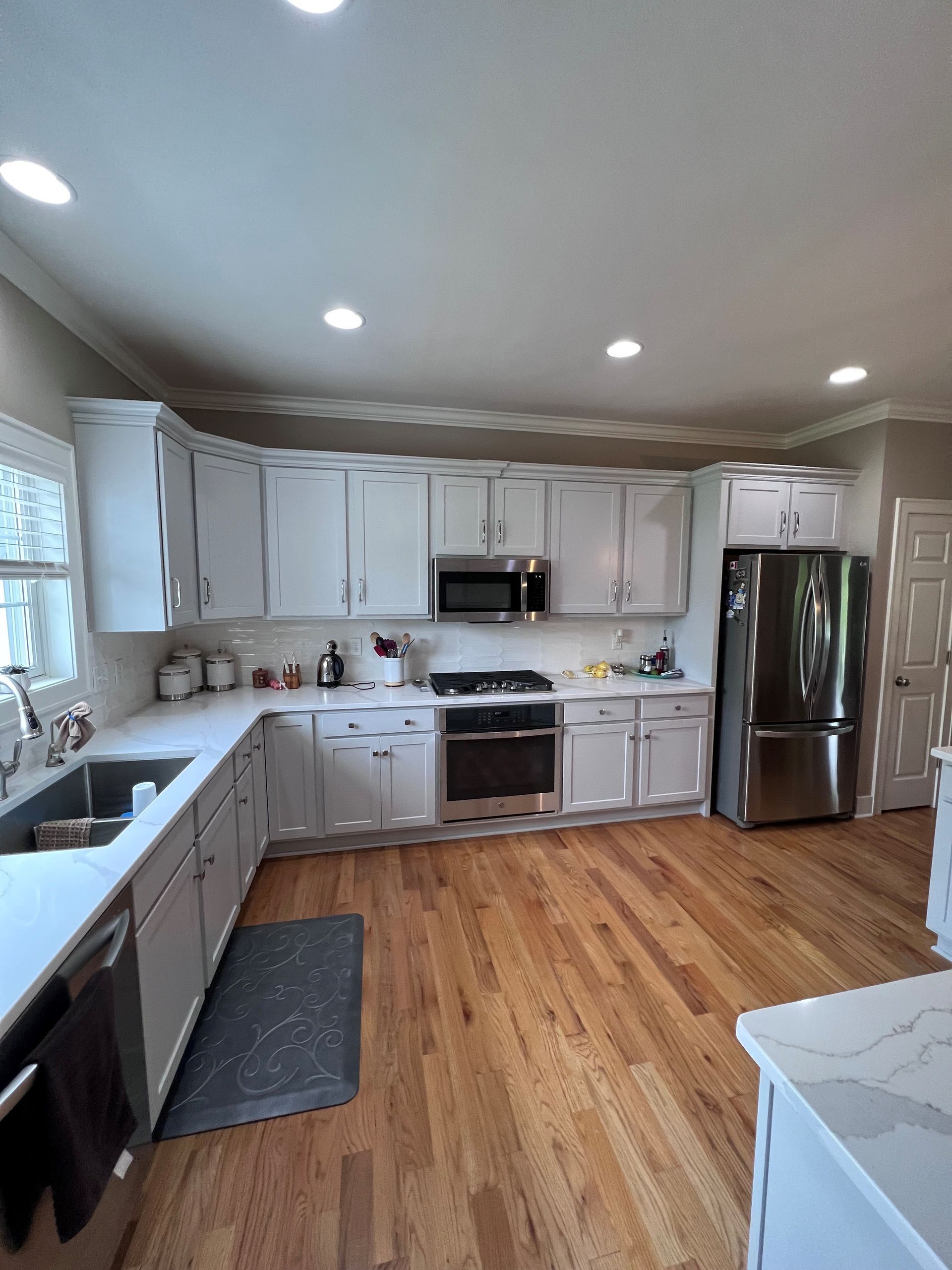 Bright kitchen with white cabinets, stainless appliances, wood floors, and recessed ceiling lights
