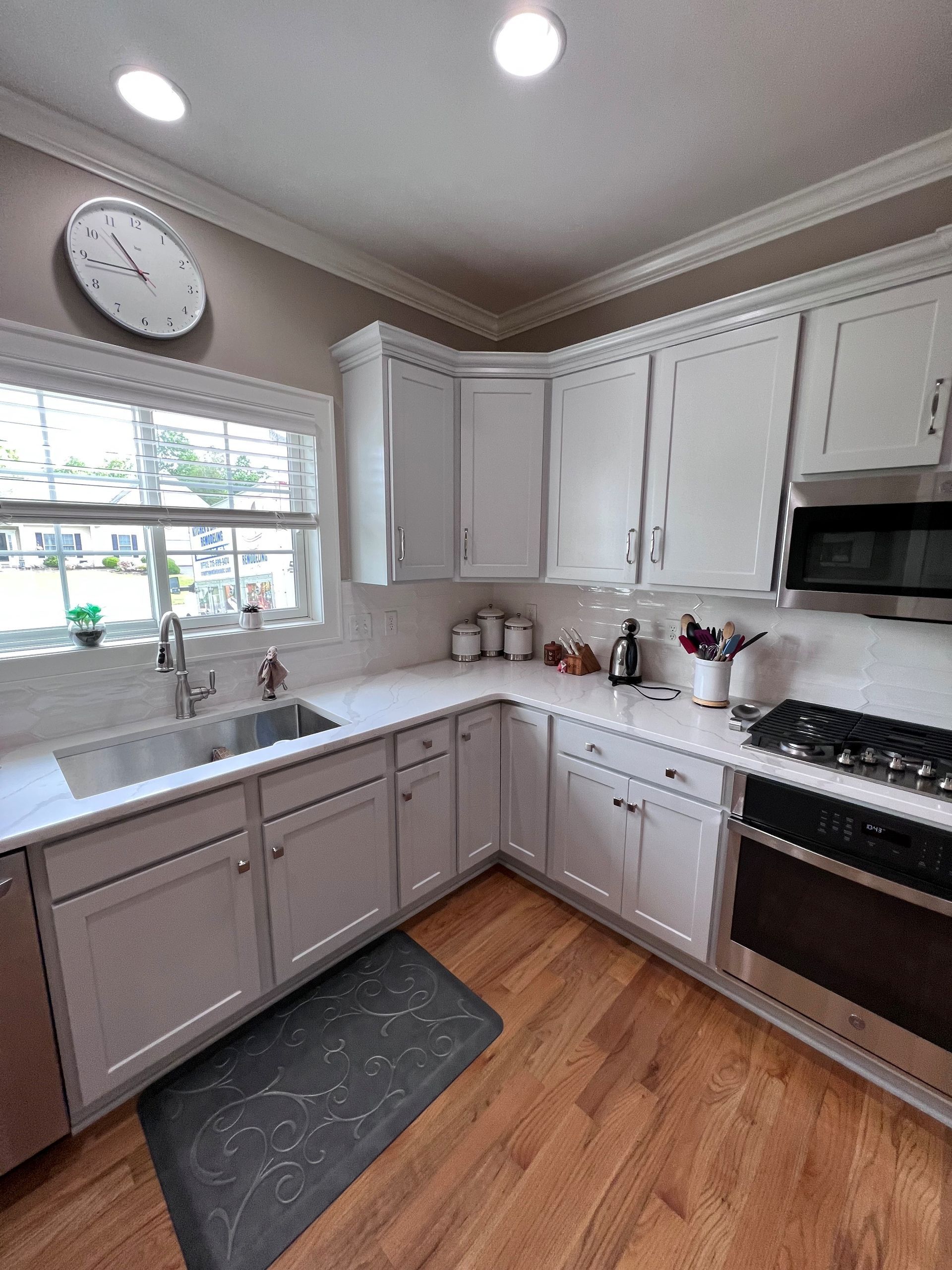 Bright white kitchen with wood floors, window over sink, and stainless steel appliances