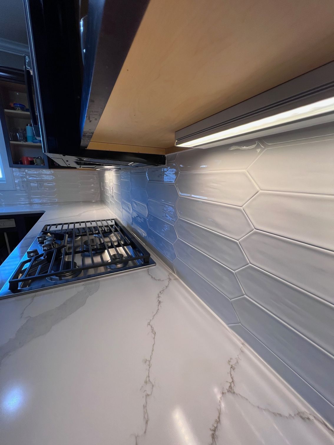Modern kitchen countertop with gas stove, marble-look surface, hex tile backsplash, and under-cabinet lighting