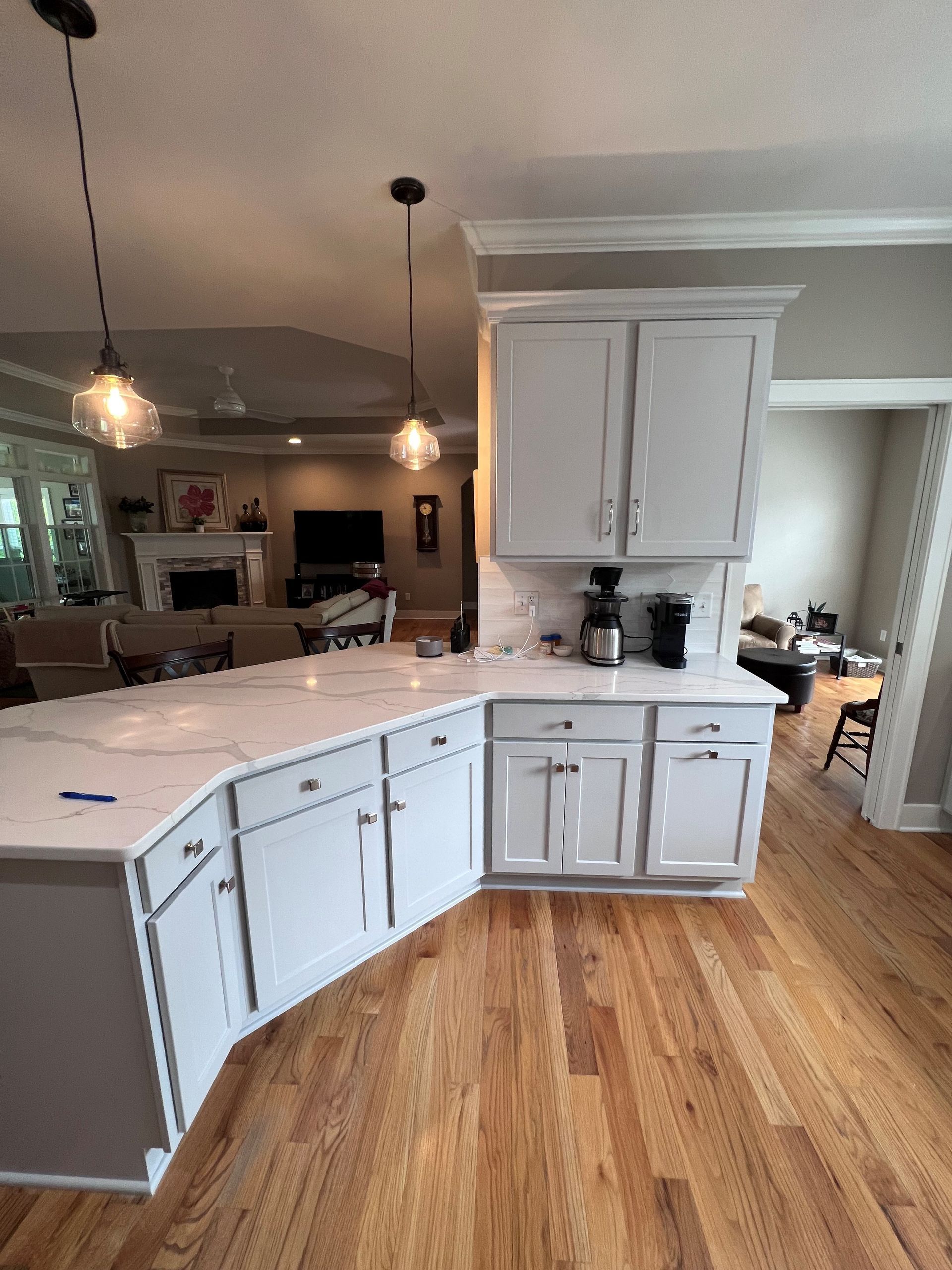 Bright kitchen with white cabinets, marble island, wood floor, and pendant lights connecting to dining area.