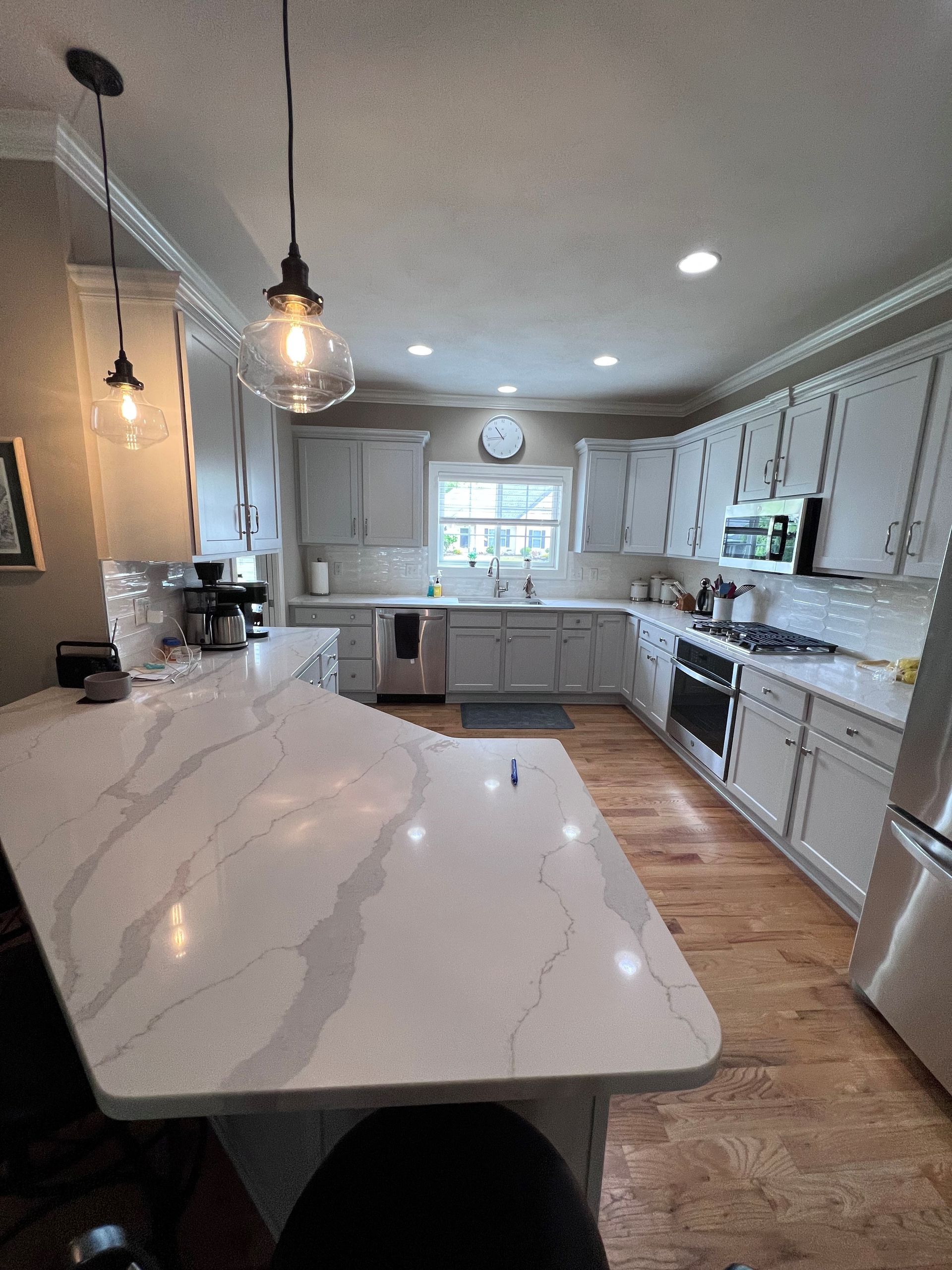 Bright white kitchen with marble island, pendant lights, and stainless-steel appliances
