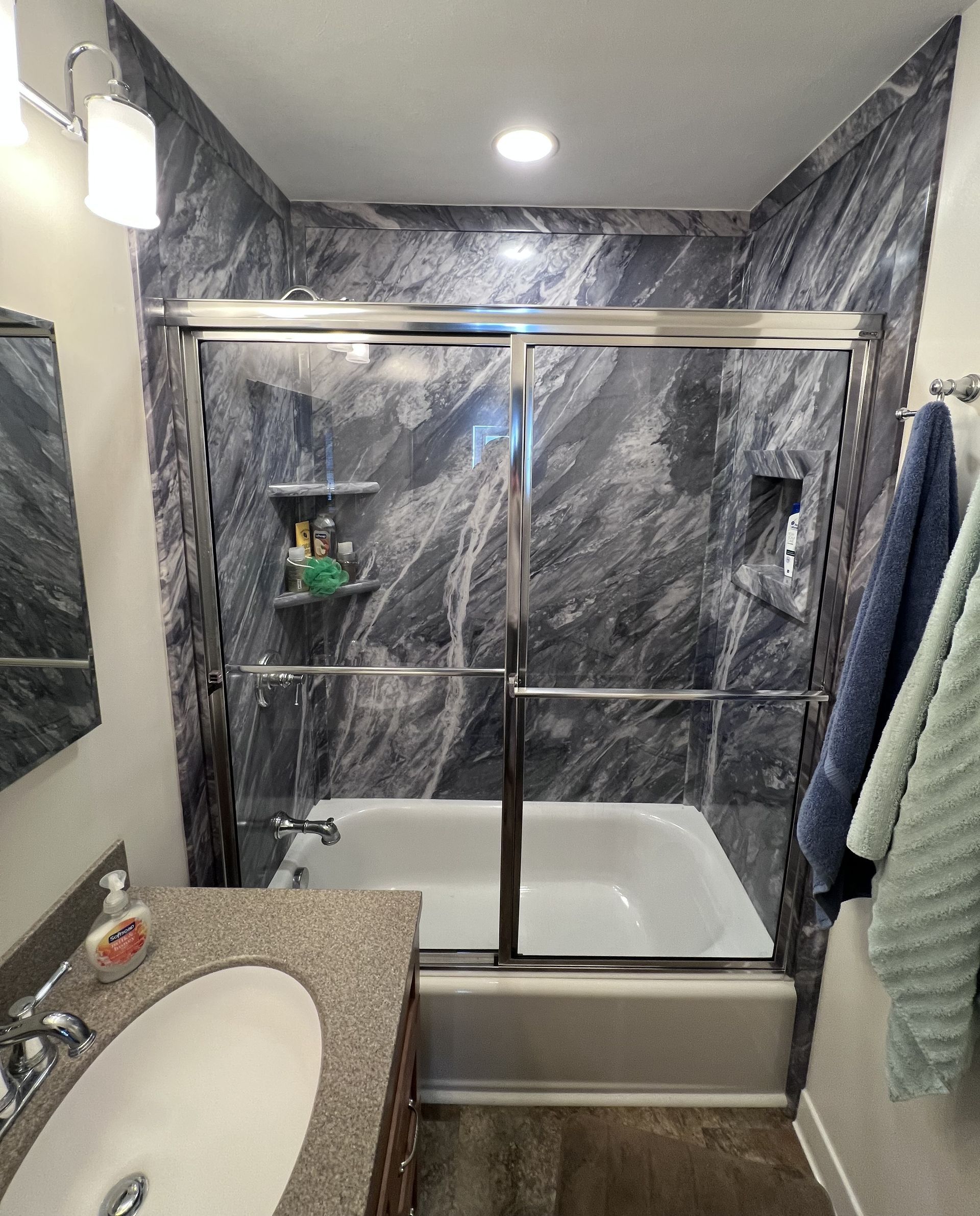 Small bathroom with a marble-pattern shower, glass sliding doors, and a white tub.