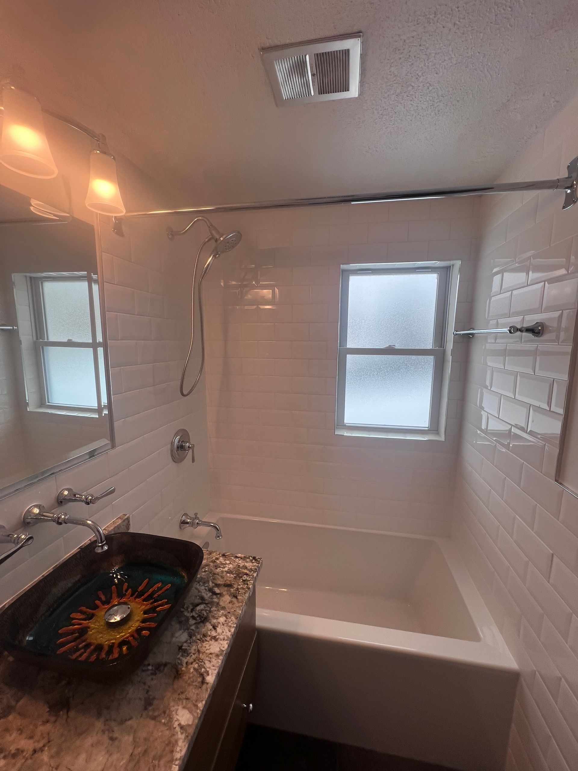 White tiled bathroom with a bathtub, sink, wall mirror, and shower fixtures.