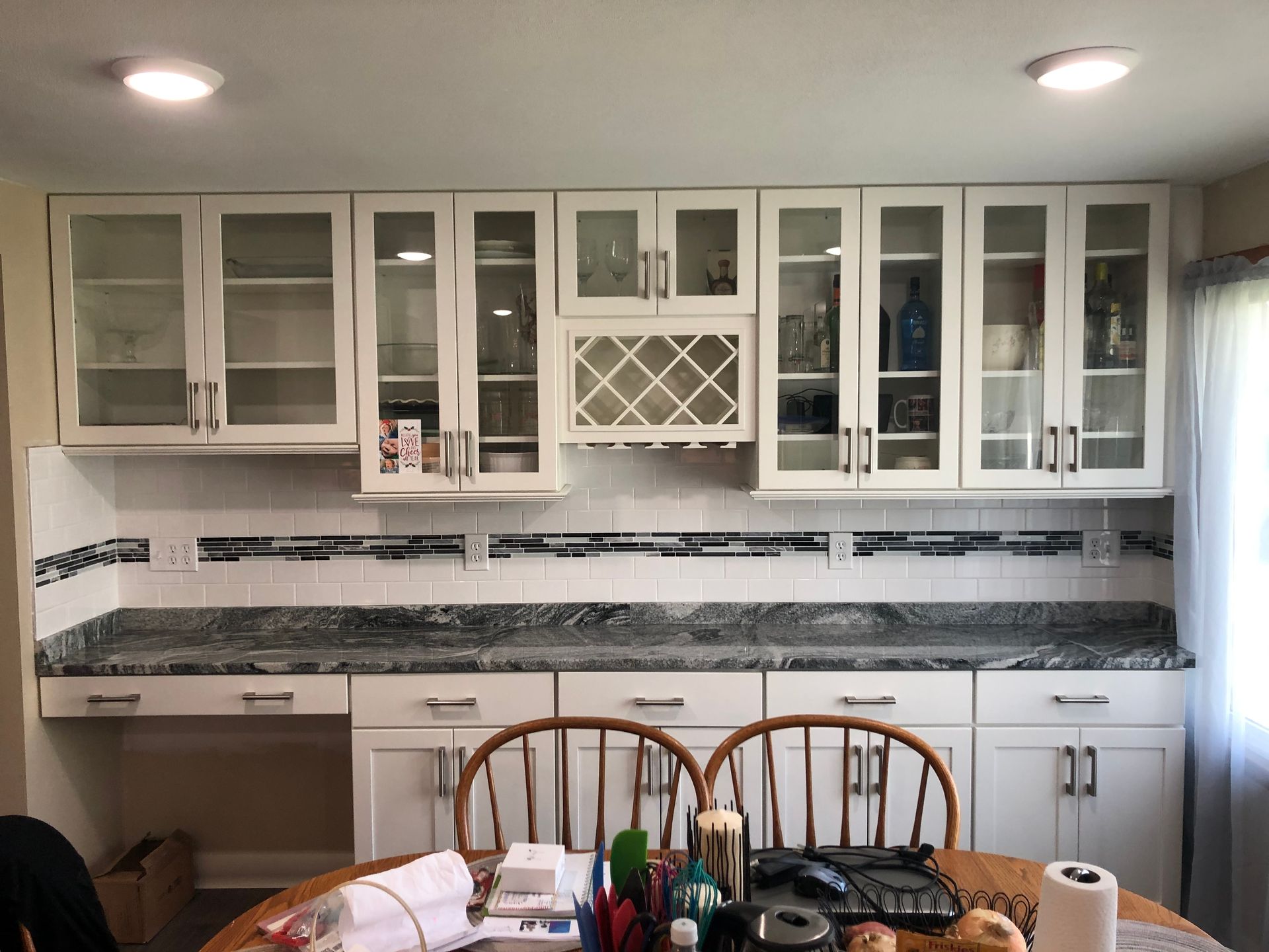 Modern kitchen with white cabinets, granite counters, tiled backsplash, and a dining table in front.
