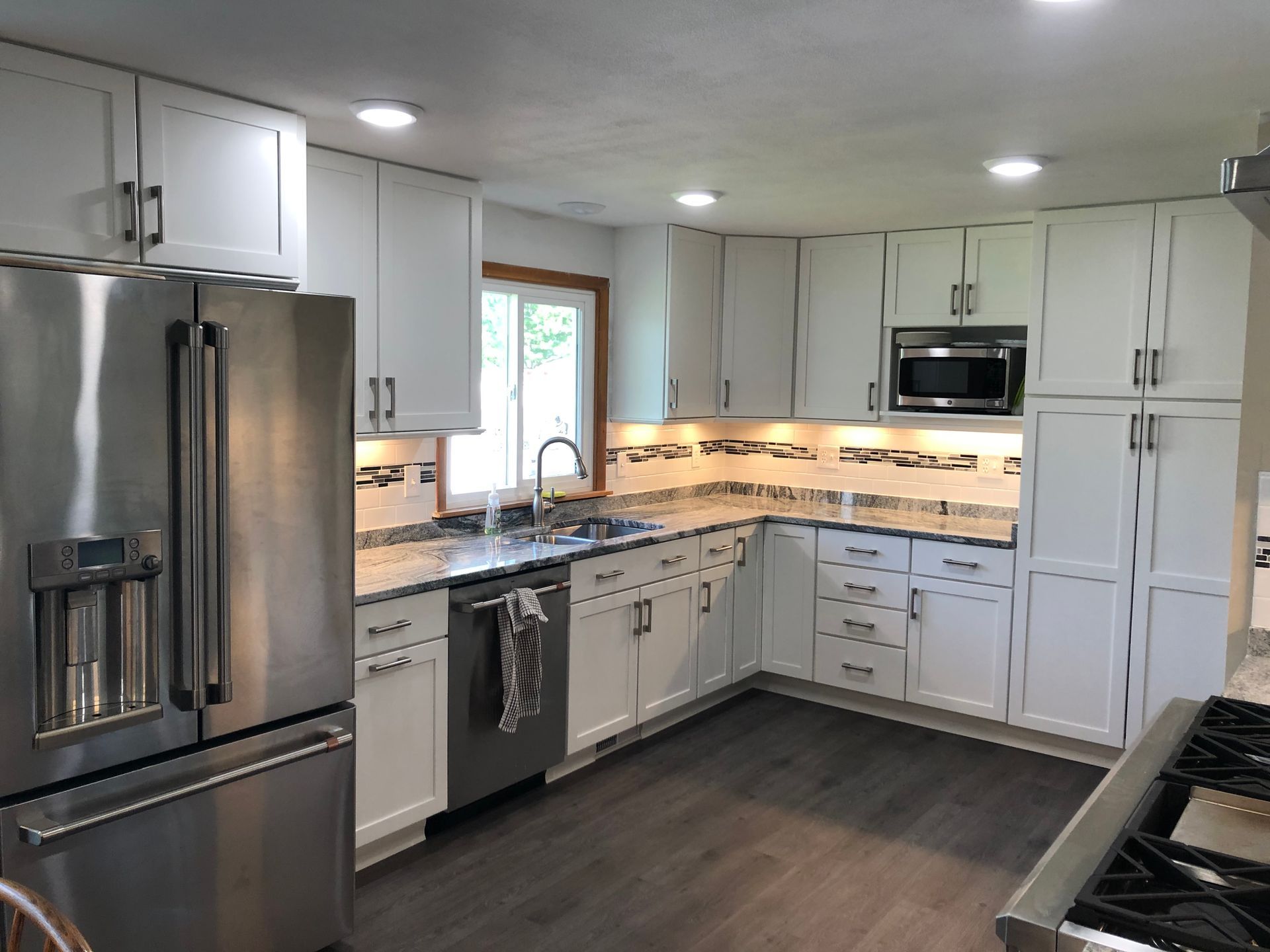 Modern kitchen with stainless steel appliances, white cabinets, gray countertops, and dark wood flooring.