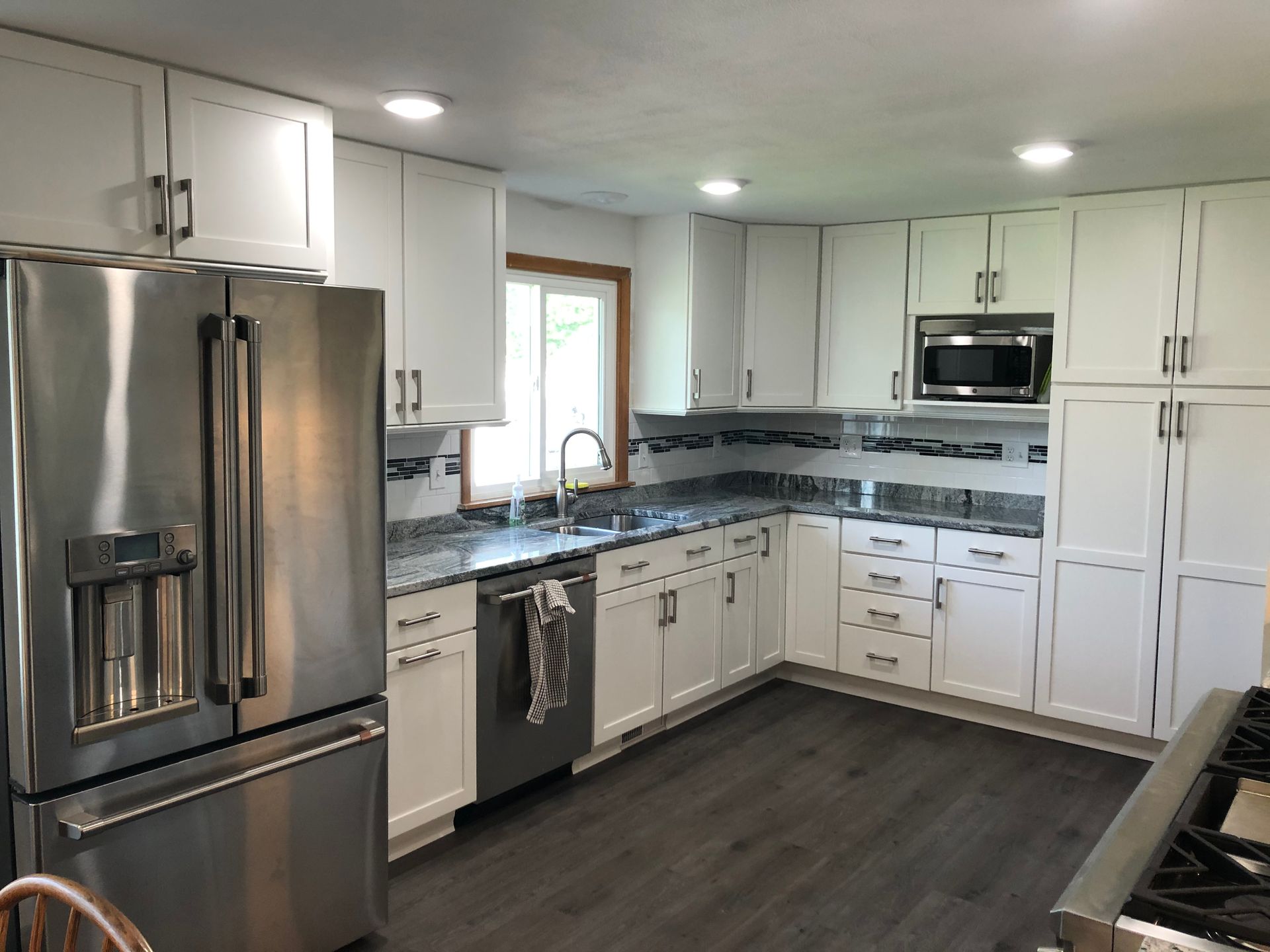 Bright modern kitchen with white cabinets, stainless steel appliances, and dark wood floors