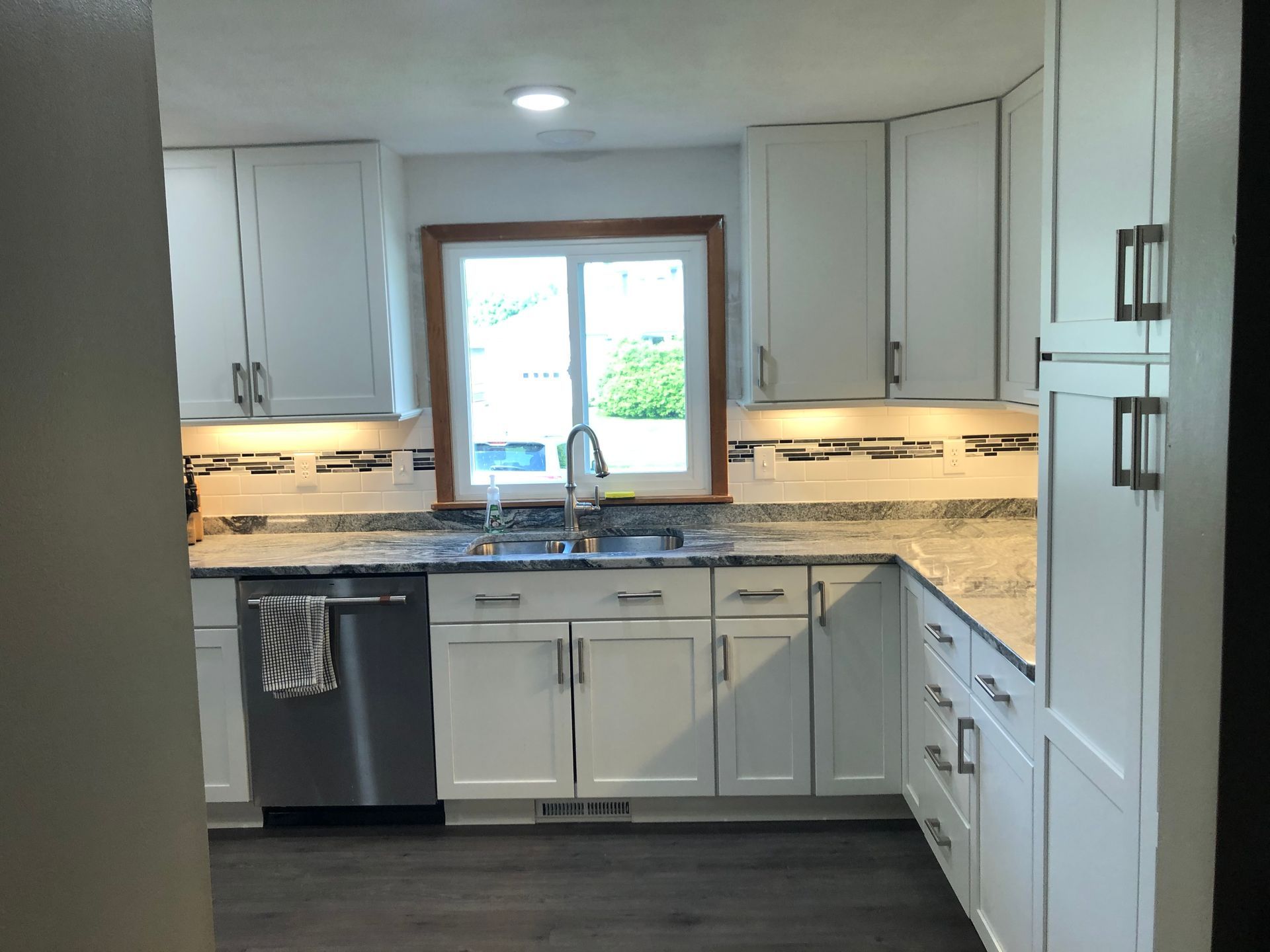 Bright white kitchen with gray counters, stainless dishwasher, and a window over the sink.