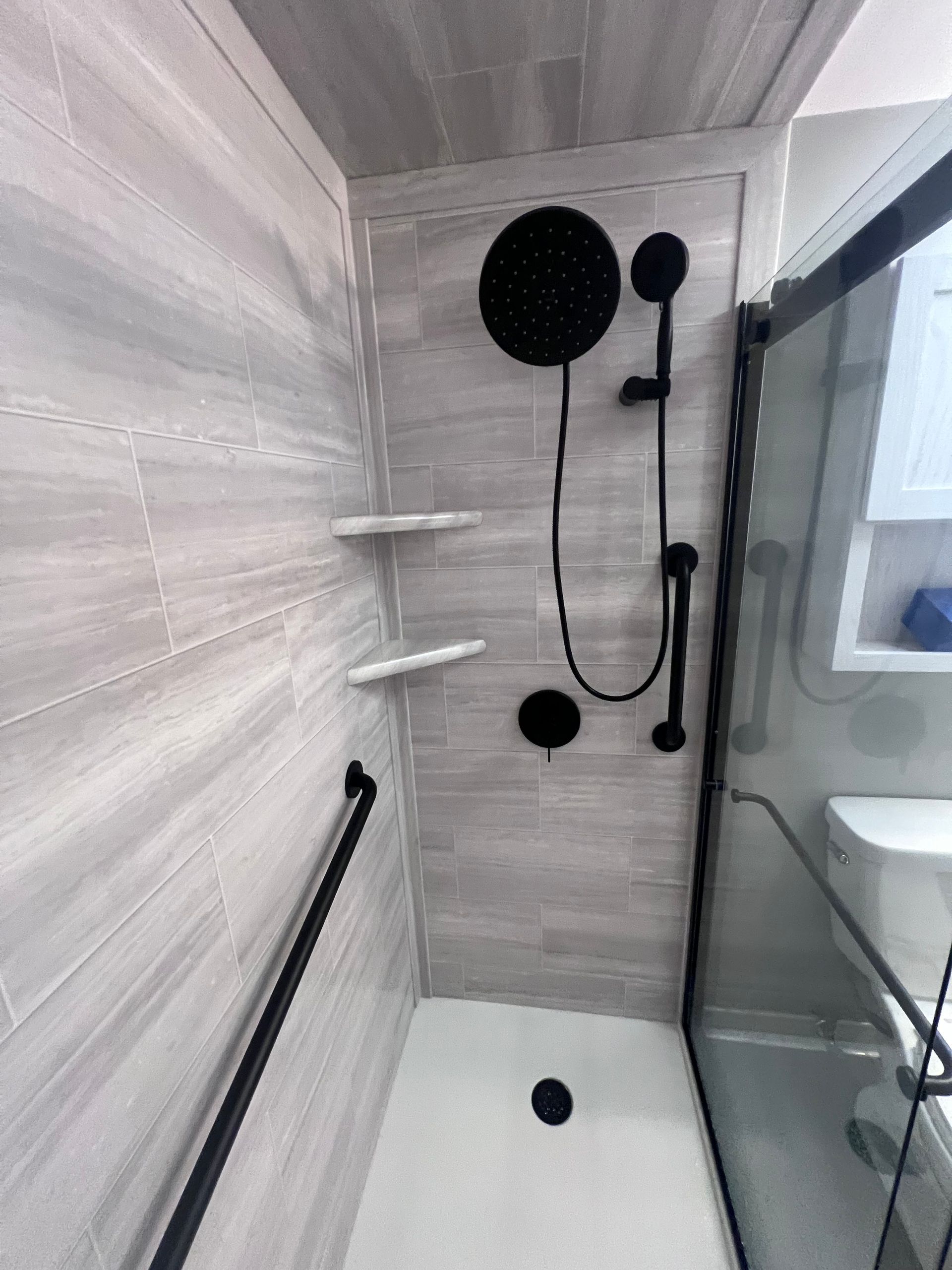 Modern shower with black fixtures, glass door, and white tile walls
