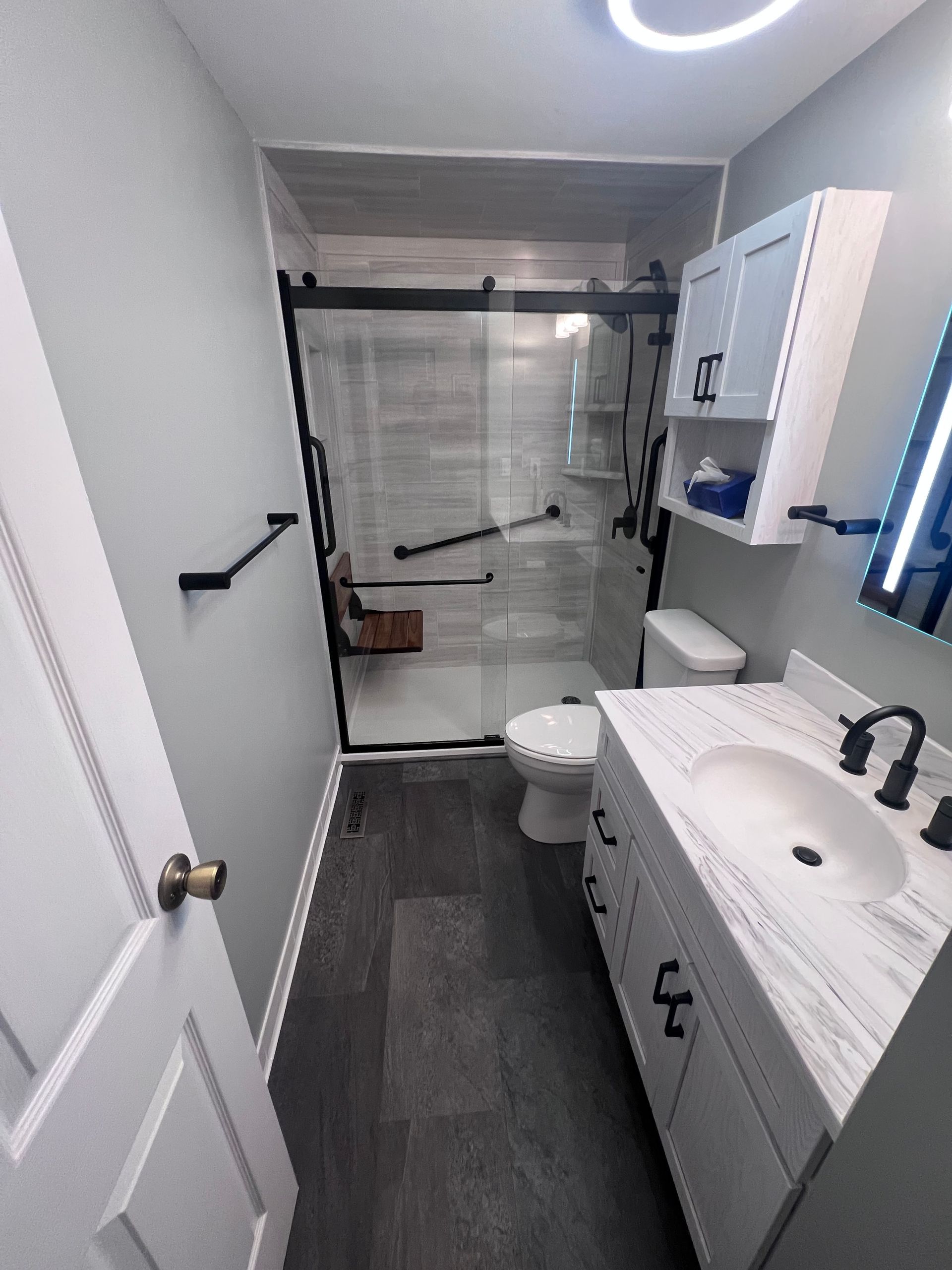 Narrow bathroom with white vanity, toilet, shower curtain, and dark floor mats.