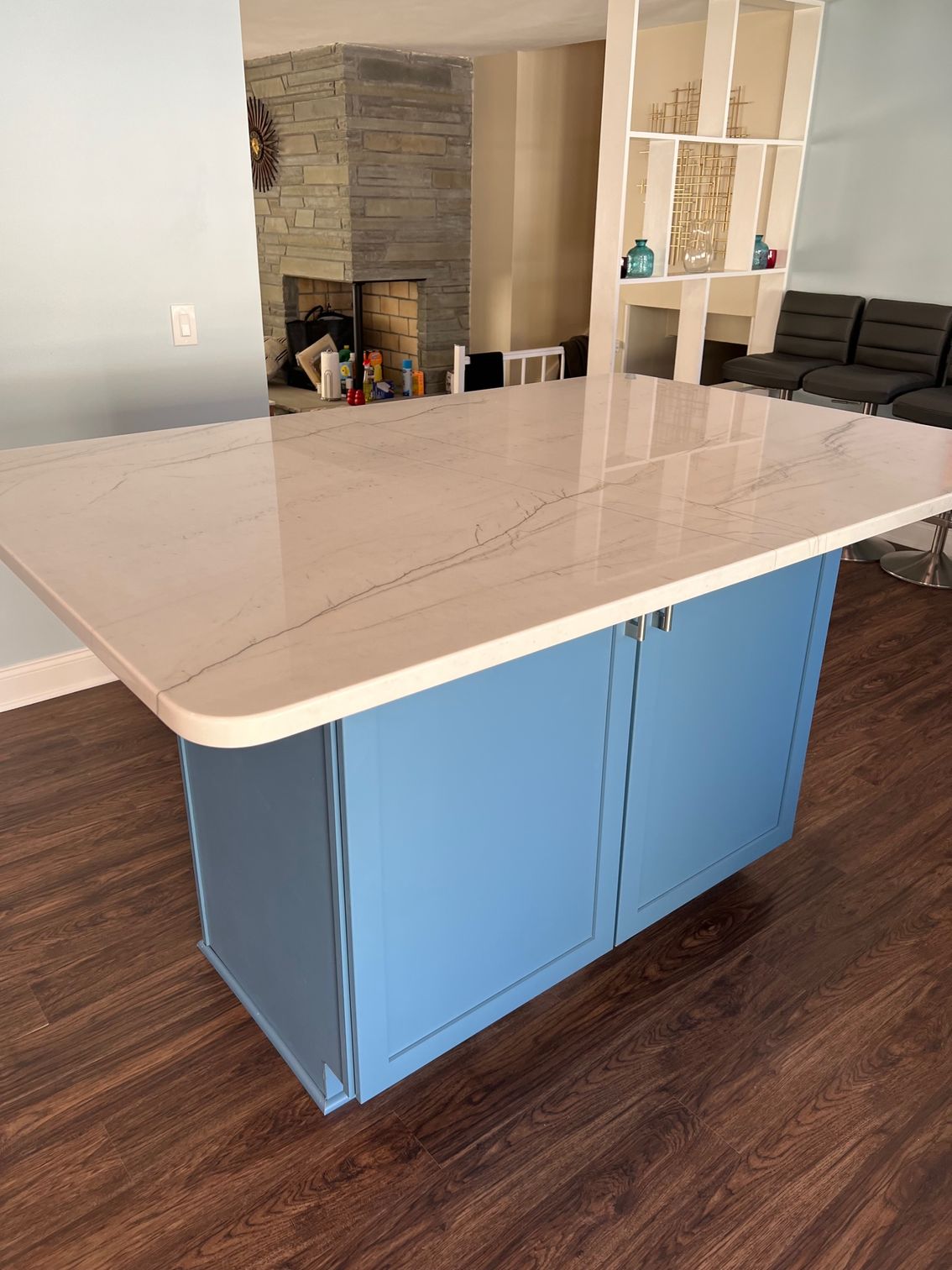 Blue kitchen island with white countertop in a living room with dark wood floors and a fireplace.