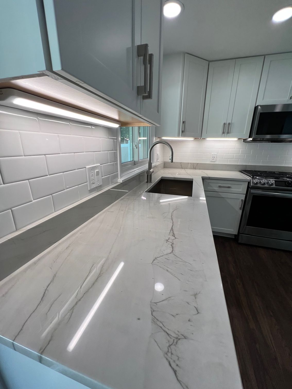 Modern kitchen with white marble countertops, gray cabinets, subway tile backsplash, and under-cabinet lighting