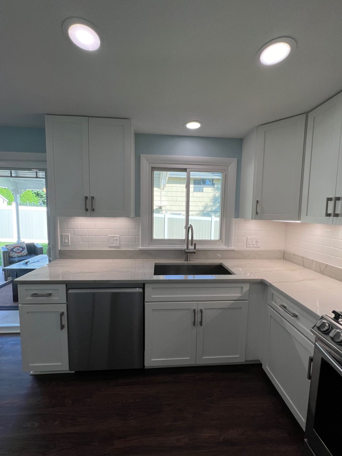 Modern kitchen with gray cabinets, stainless appliances, dark floor, and window over the sink