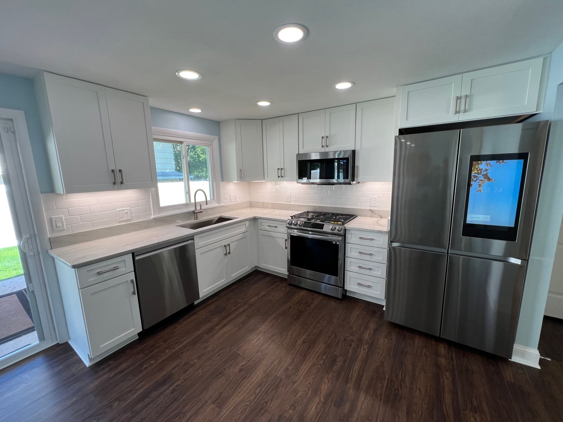 Bright modern kitchen with white cabinets, stainless steel appliances, dark wood floors, and a window over the sink