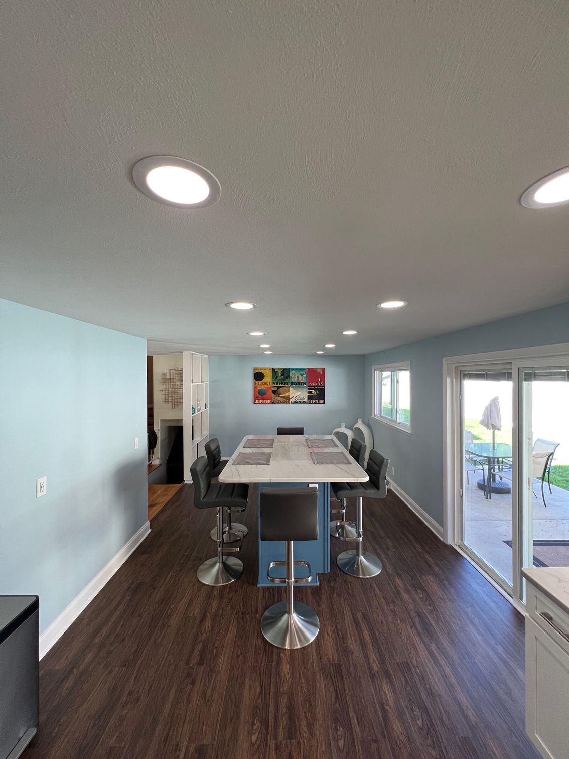 Modern dining room with a long table, gray chairs, blue walls, and sliding glass doors.