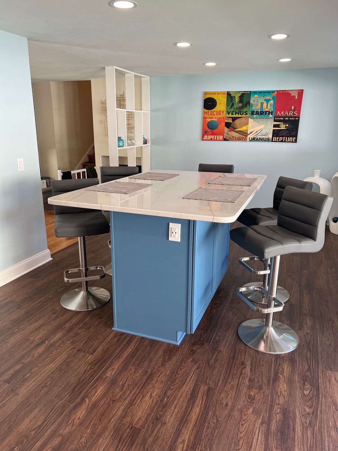 Modern kitchen with blue island, two bar stools, wood floors, and colorful wall art
