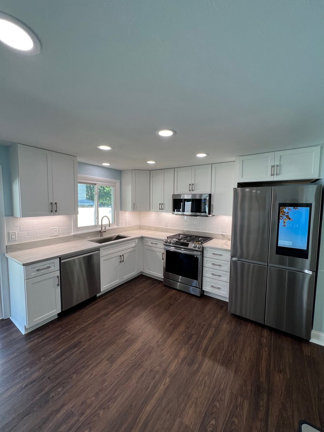 Bright modern kitchen with white cabinets, stainless appliances, dark wood floor, and gray countertop.
