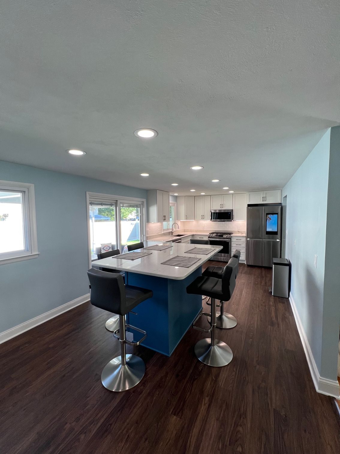 Modern kitchen with blue island, bar stools, dark wood floors, and stainless steel appliances