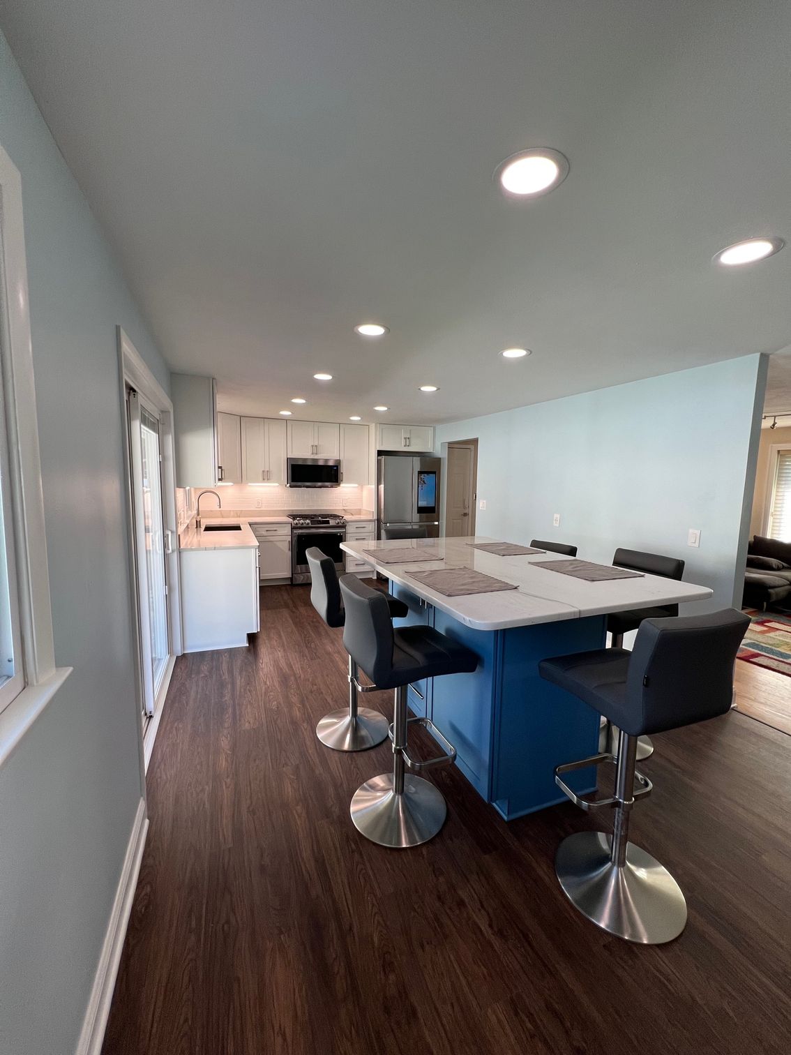 Modern kitchen with blue island, bar stools, white cabinets, and dark wood floor