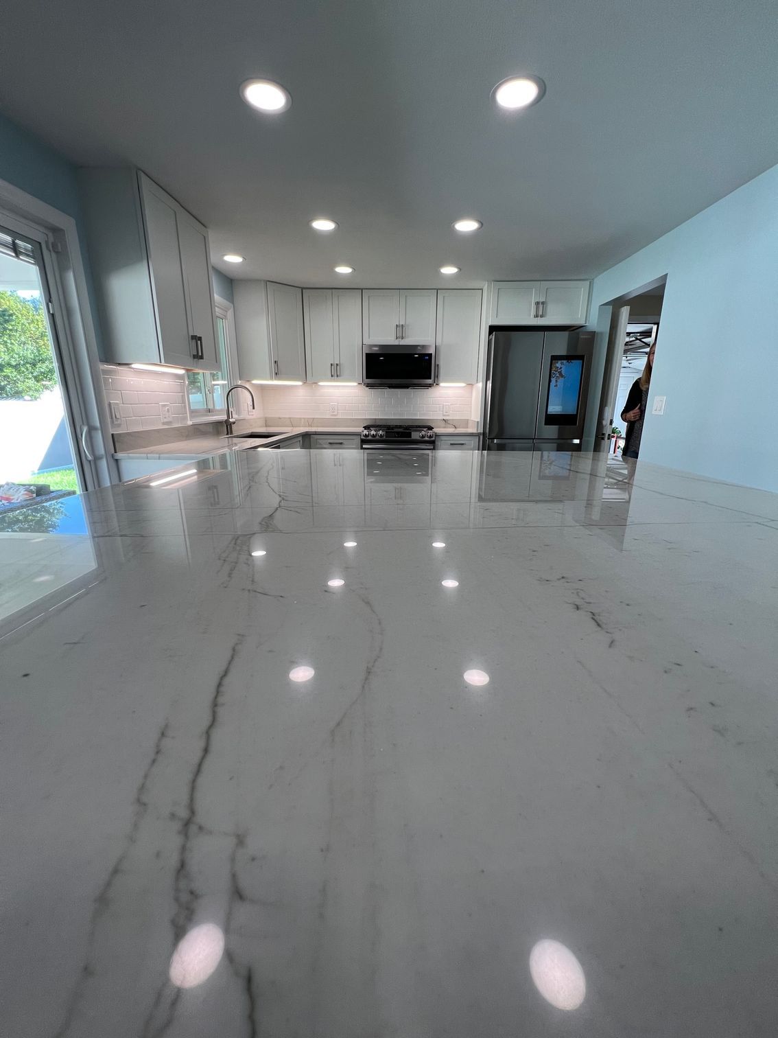 Bright modern kitchen with glossy white floors, recessed lights, and light wood cabinetry