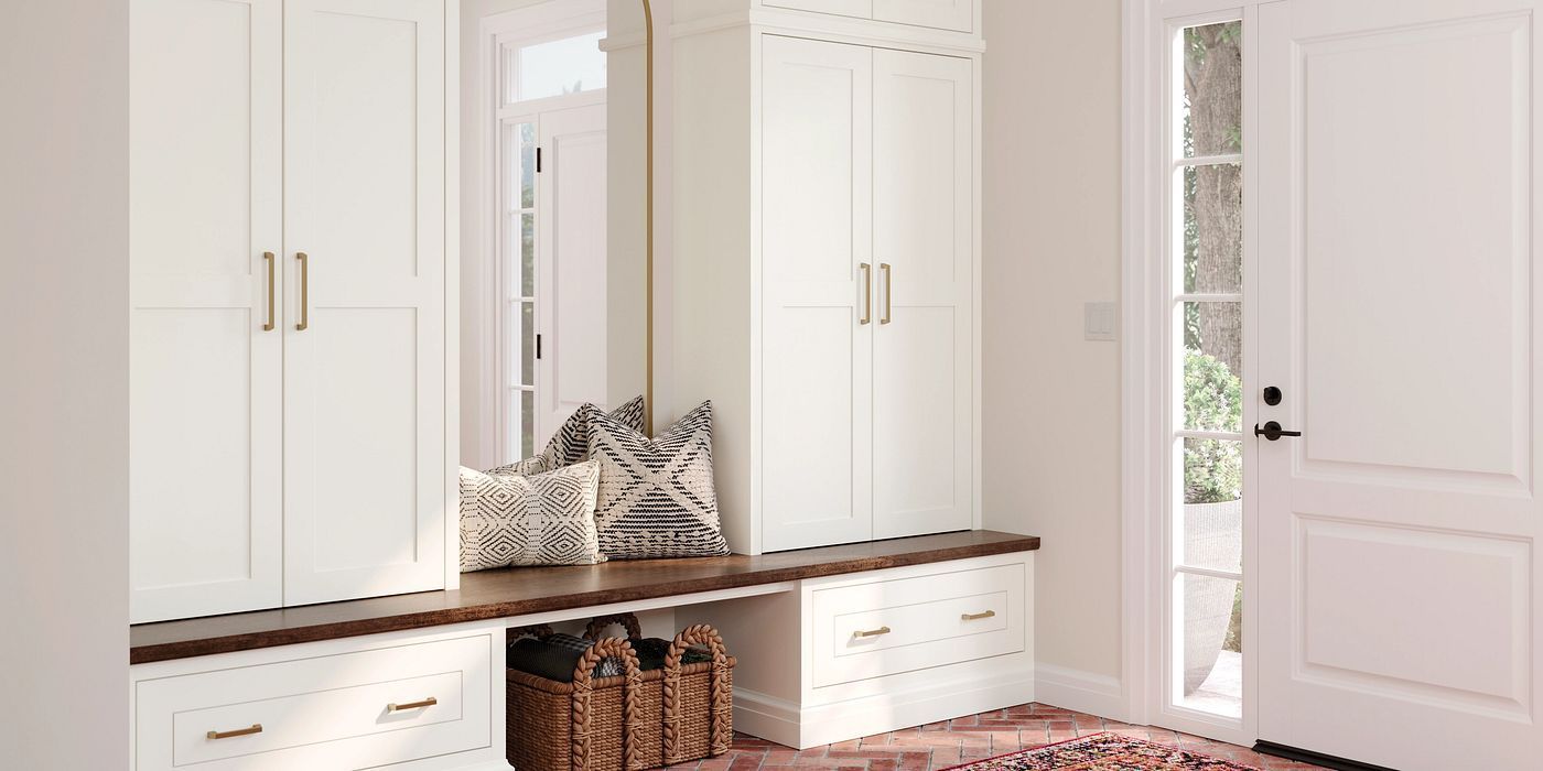 Bright mudroom with white built-in cabinets, bench, wicker baskets, and a glass door to outside.