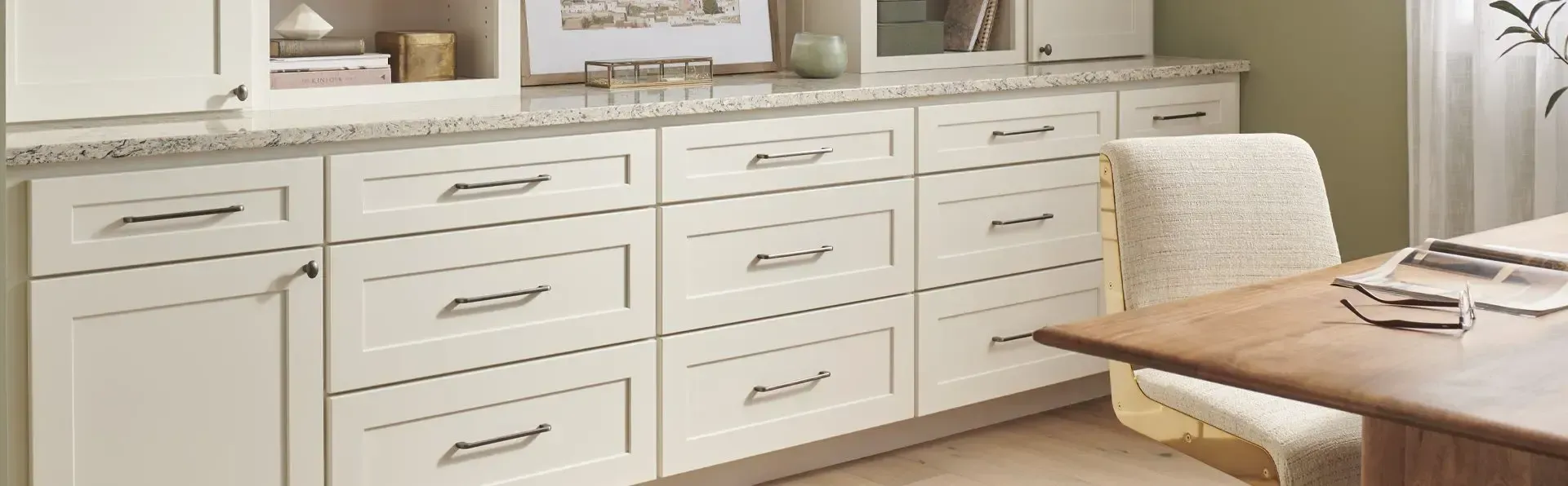 White kitchen with built-in cabinets, marble countertop, and a dining table with chairs.