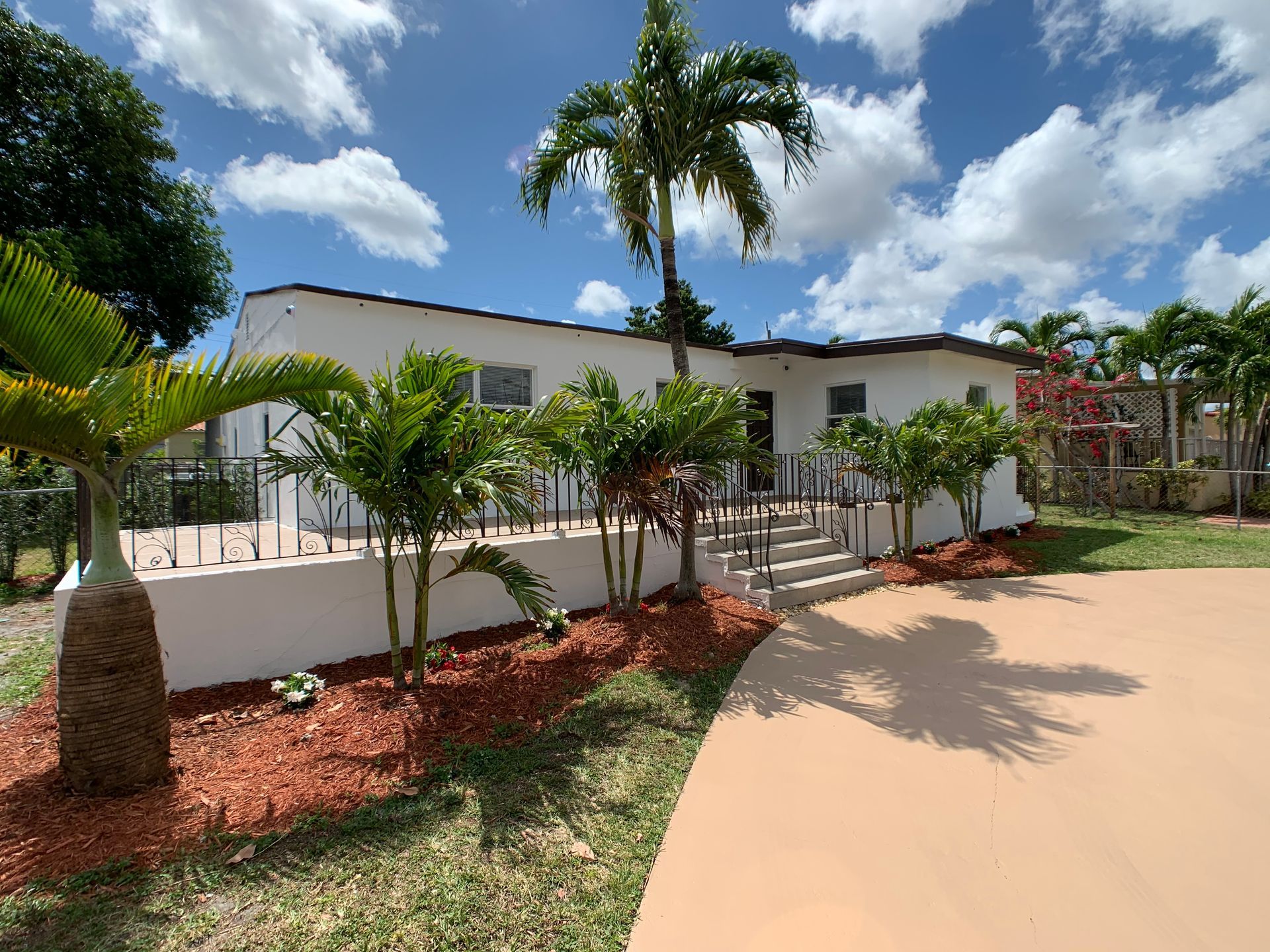 White house with red mulch and palm trees.