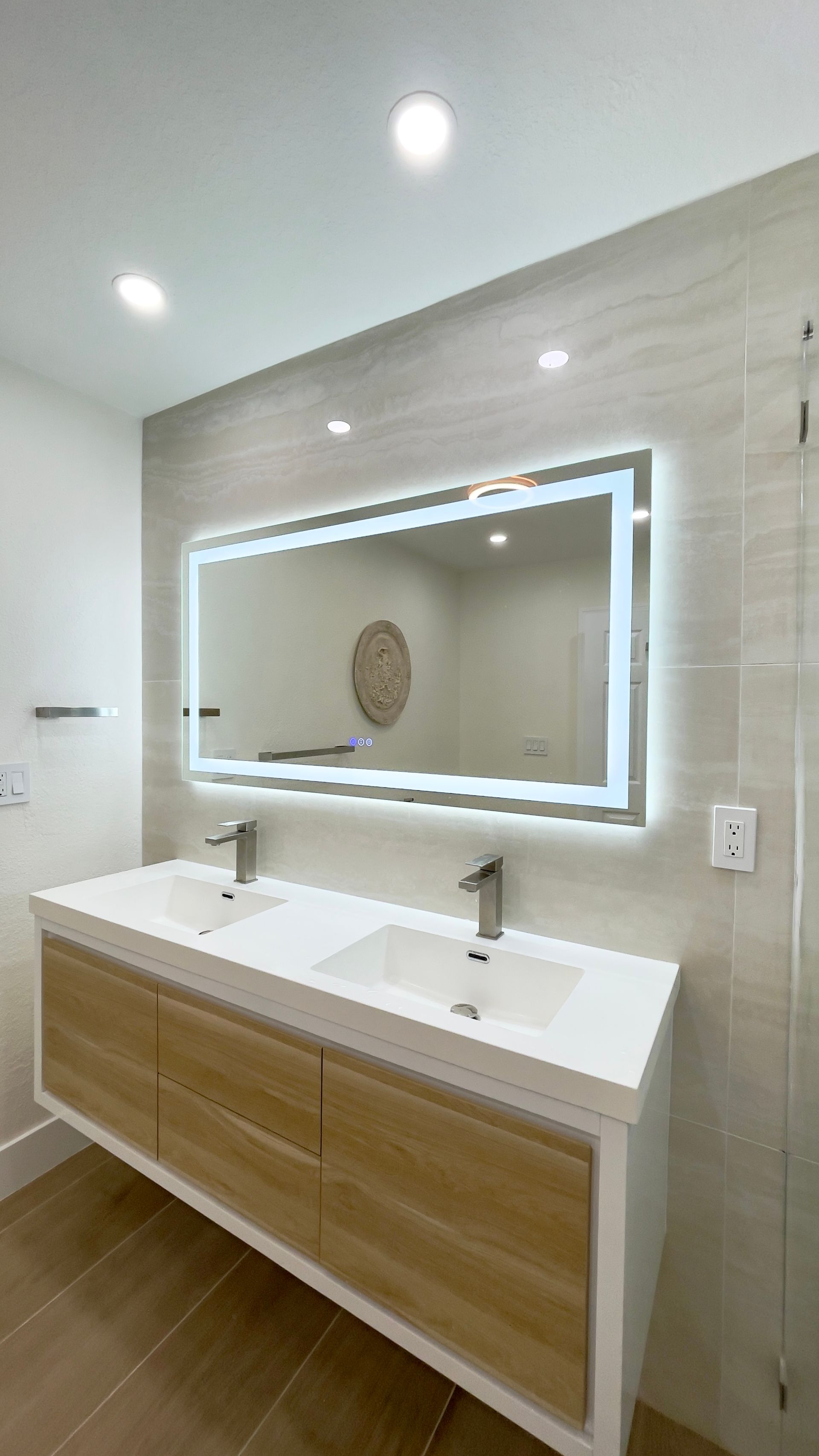 Modern bathroom with double vanity, lit mirror, and light-colored wood cabinets.