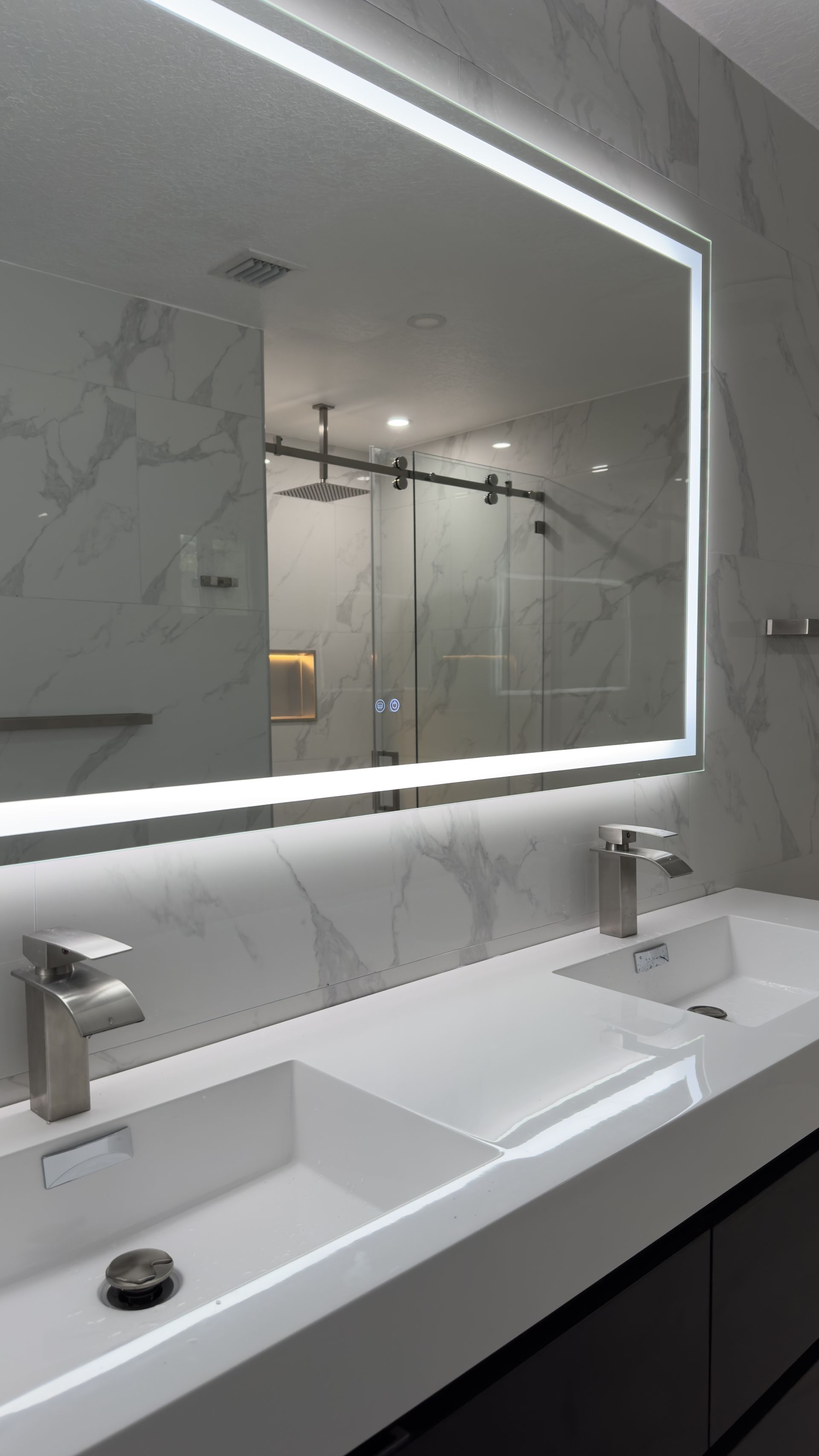 Modern bathroom with a large backlit mirror above a double sink vanity.