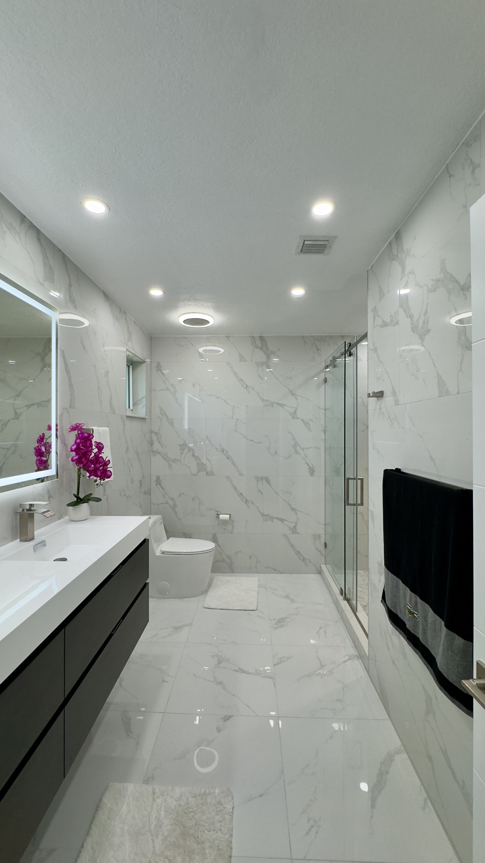 Modern white marble bathroom with a double sink vanity, shower, and toilet.